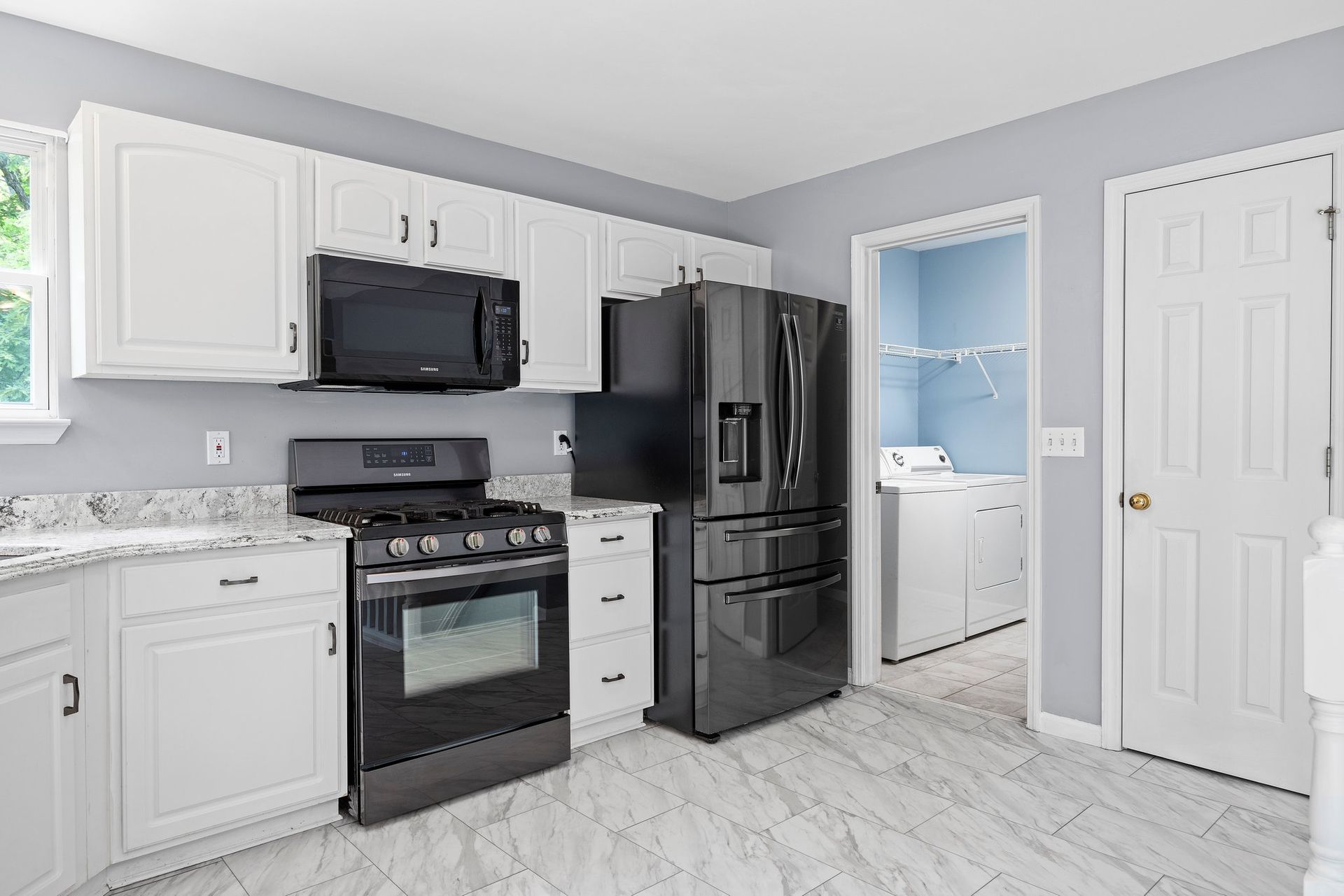 A kitchen with white cabinets , a black refrigerator , a stove , and a microwave.