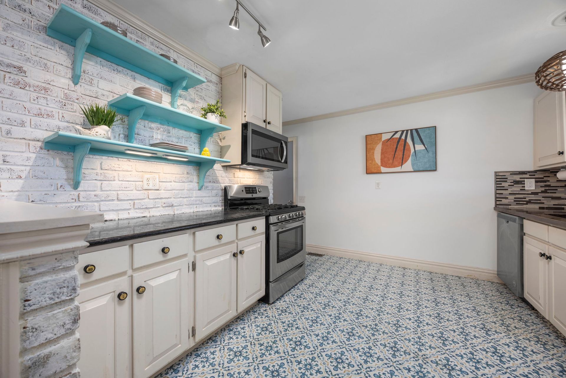 Kitchen with blue tile floor, white brick accent wall with blue shelves, and white cabinets.
