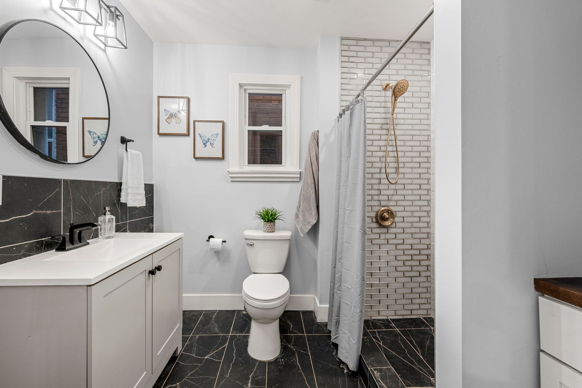 A modern bathroom with a white vanity, gray walls, and a brick-tiled shower.