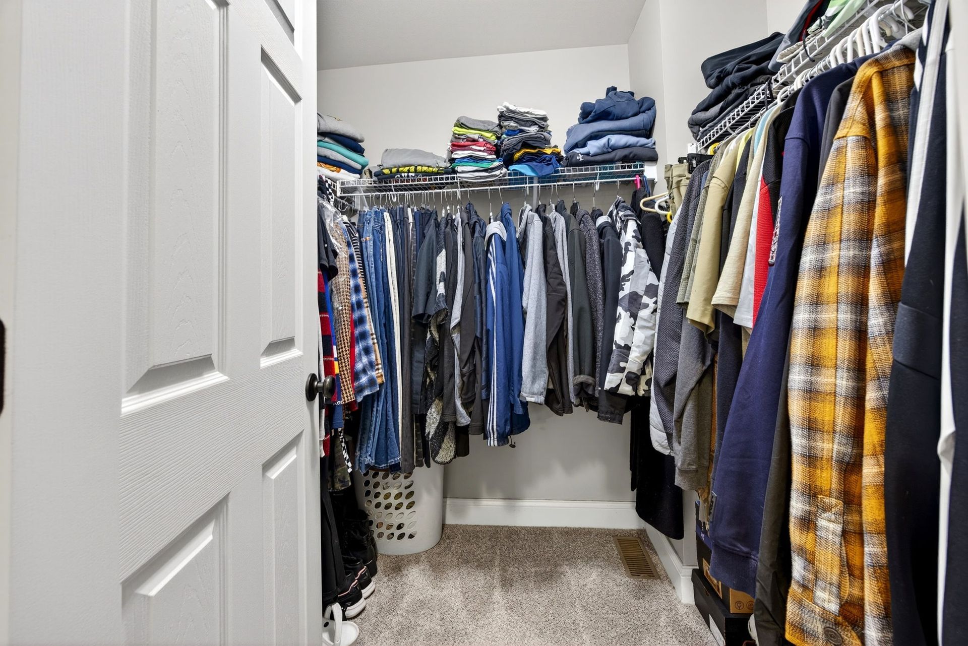 A walk-in closet with clothes hanging on racks and folded items stacked on a top shelf above.
