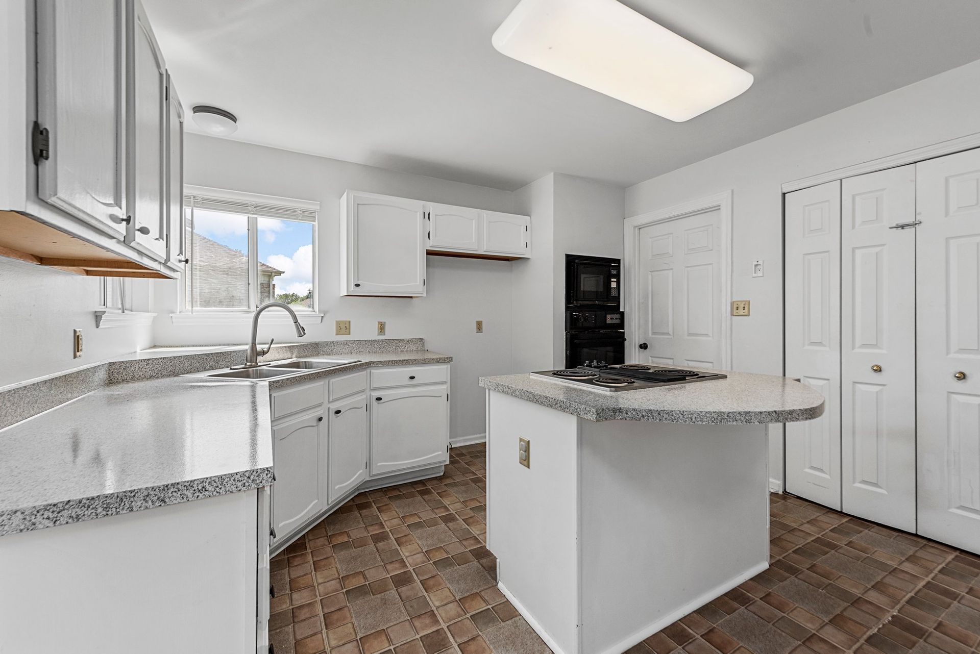 A kitchen with white cabinets , granite counter tops , and a large island.