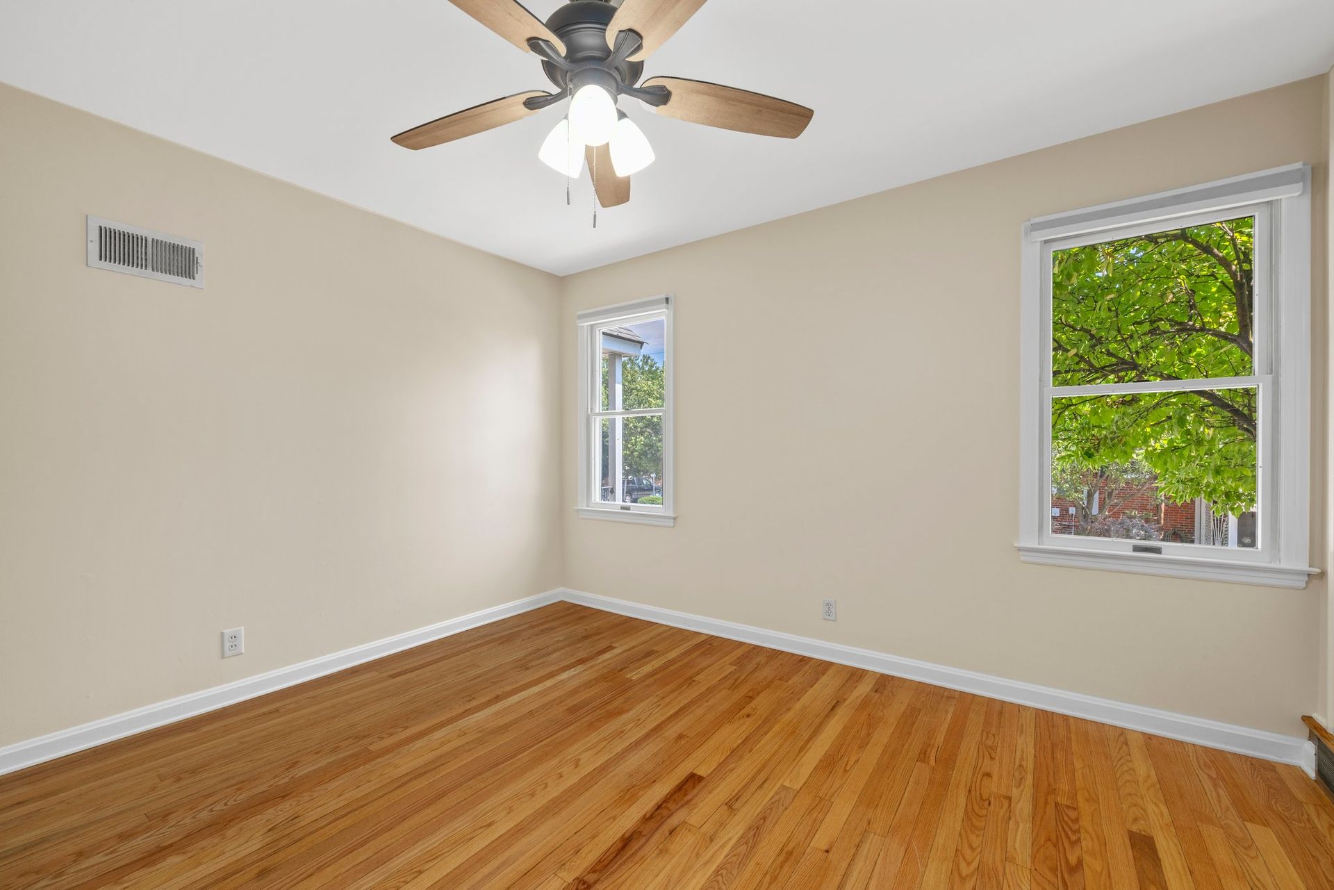 An empty bedroom with hardwood floors and a ceiling fan.