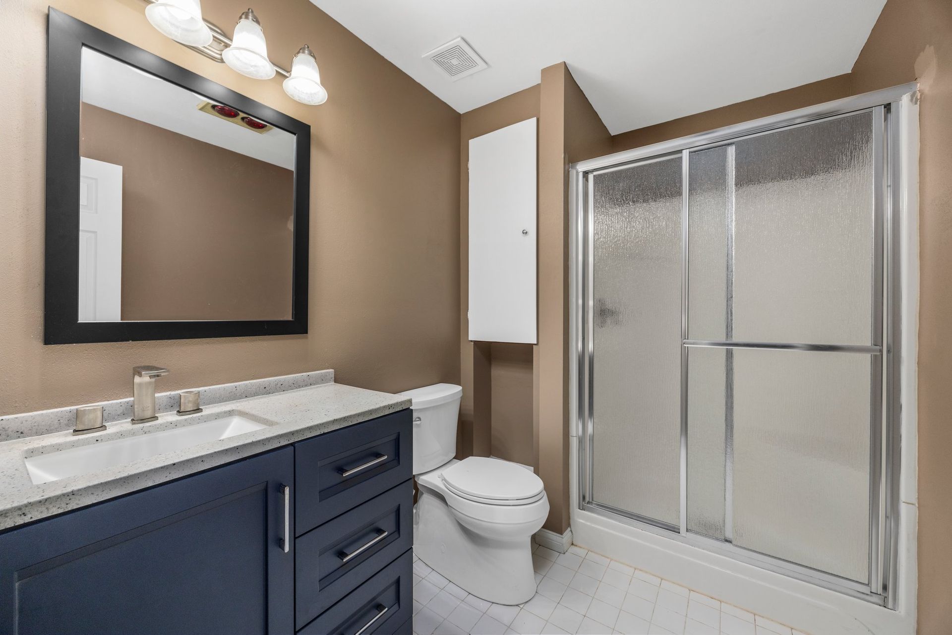 A bathroom with a toilet , sink , mirror and shower stall.