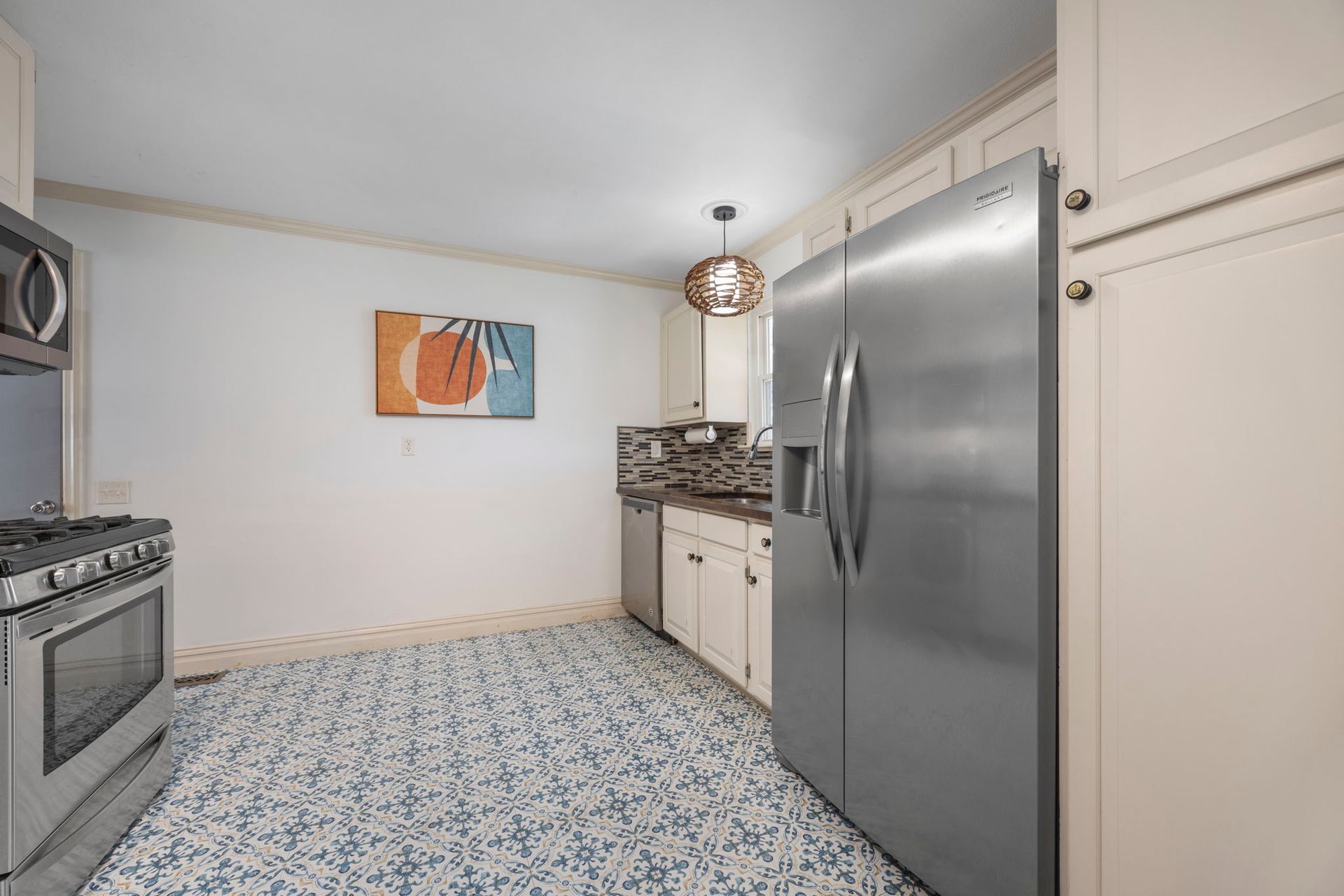 Kitchen with stainless steel appliances, white cabinets, blue patterned floor, and an abstract wall art.