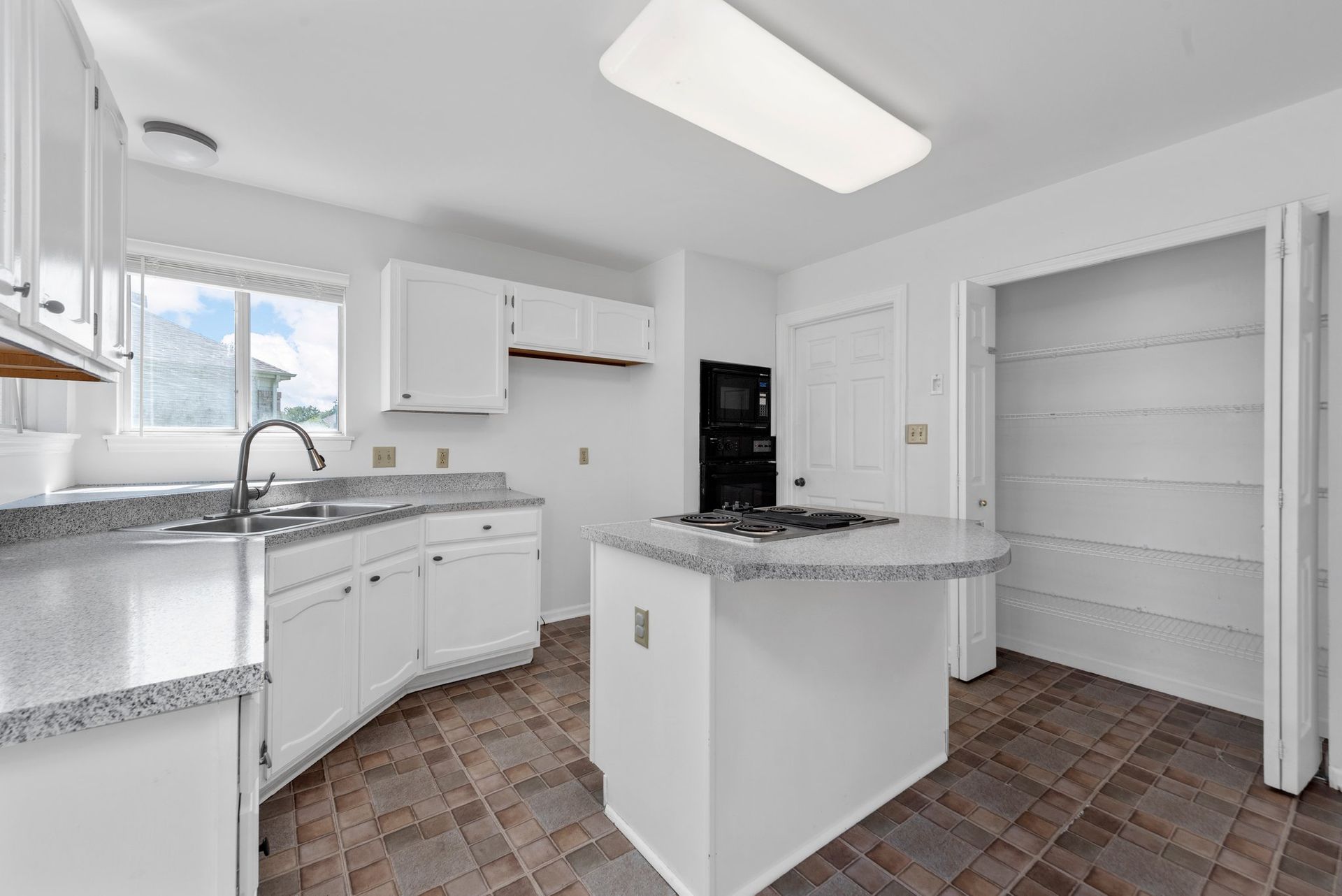 An empty kitchen with white cabinets and a large island.