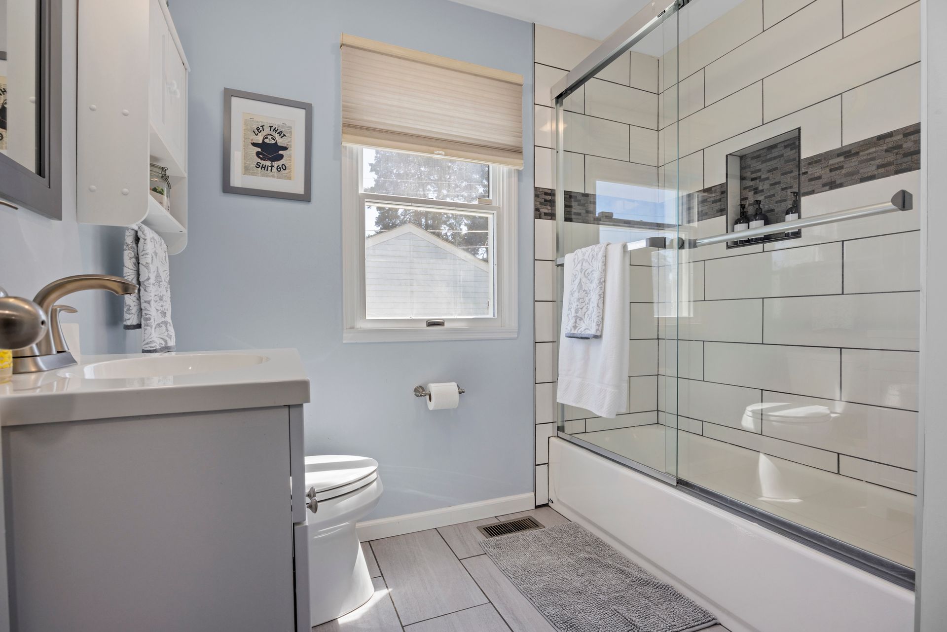A bathroom with a toilet , sink , shower and window.