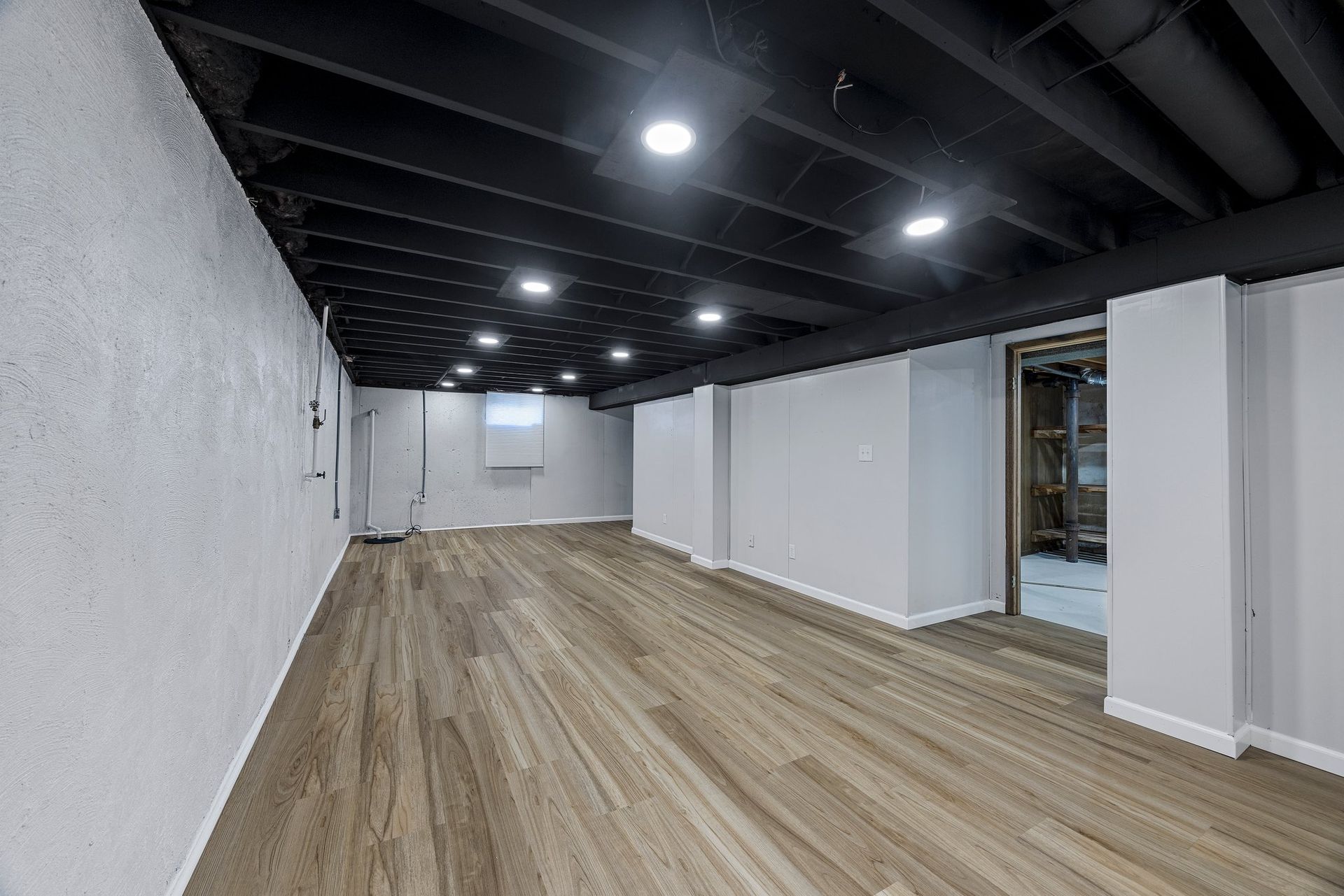 An empty basement with hardwood floors and a black ceiling.