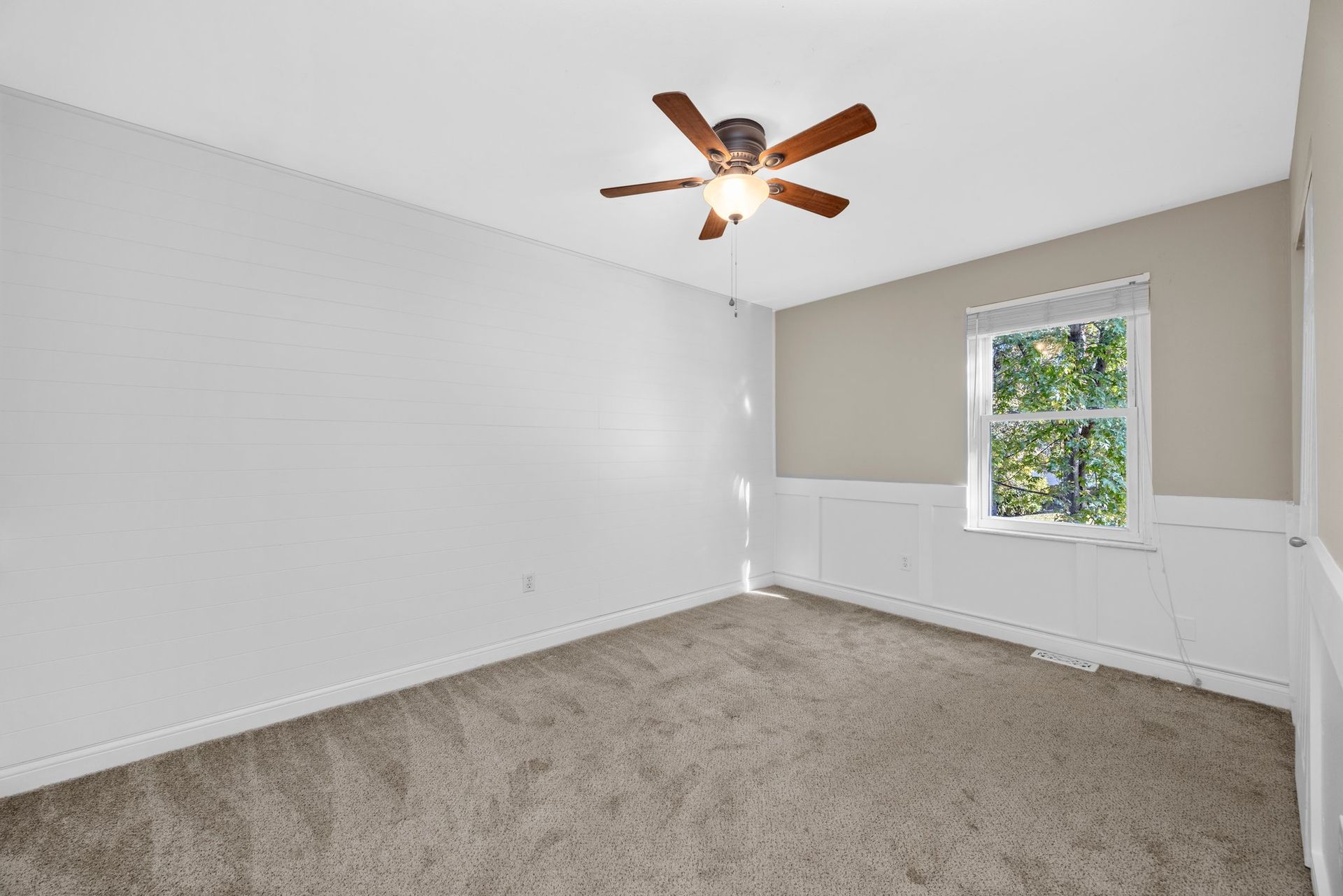 An empty bedroom with a ceiling fan and a window.