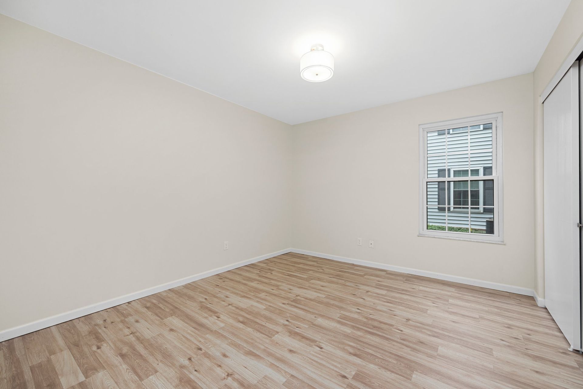 An empty bedroom with hardwood floors and a window.