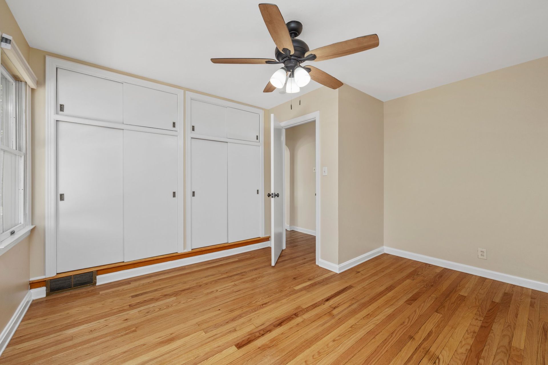 An empty bedroom with hardwood floors and a ceiling fan.