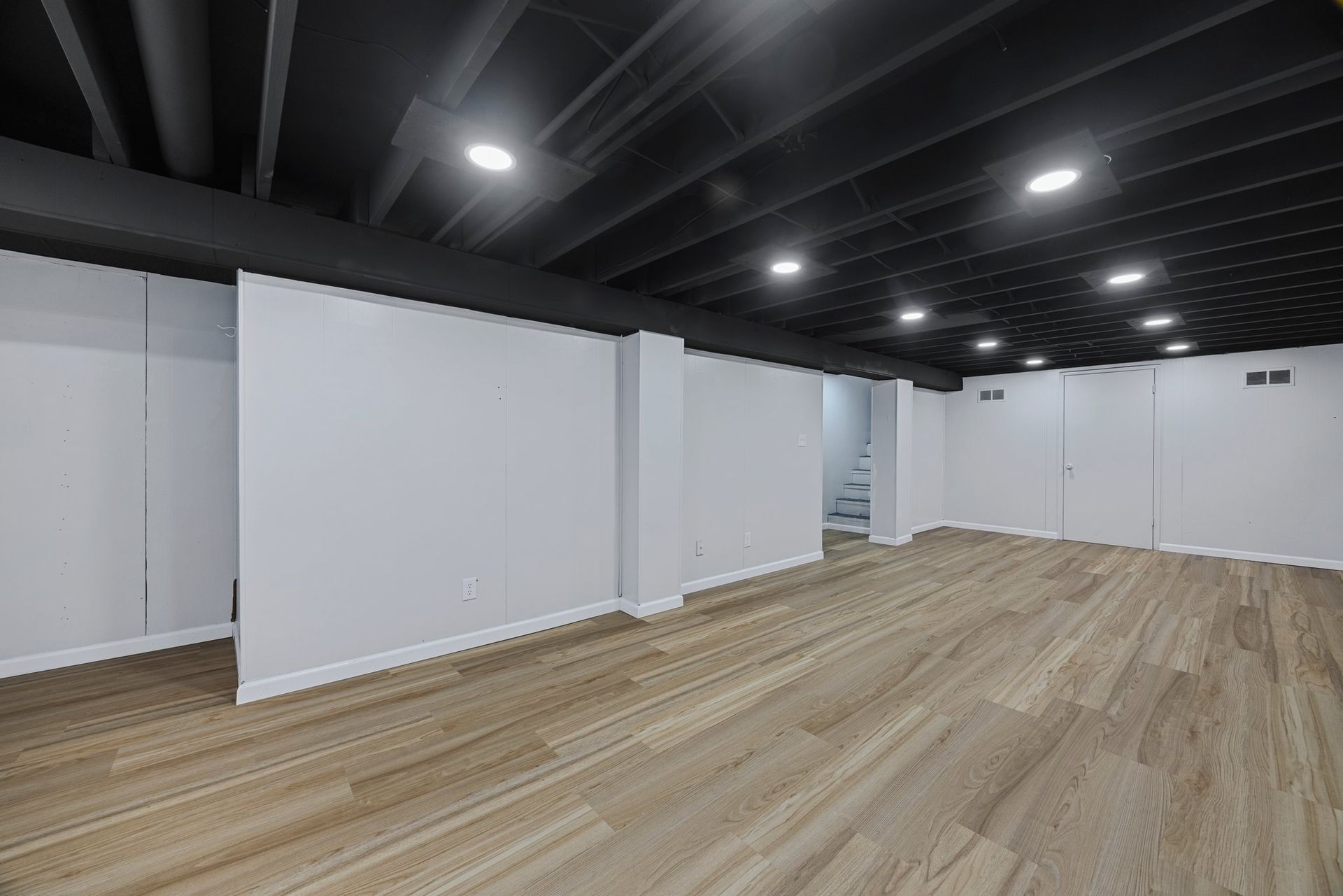 An empty basement with hardwood floors and white walls.
