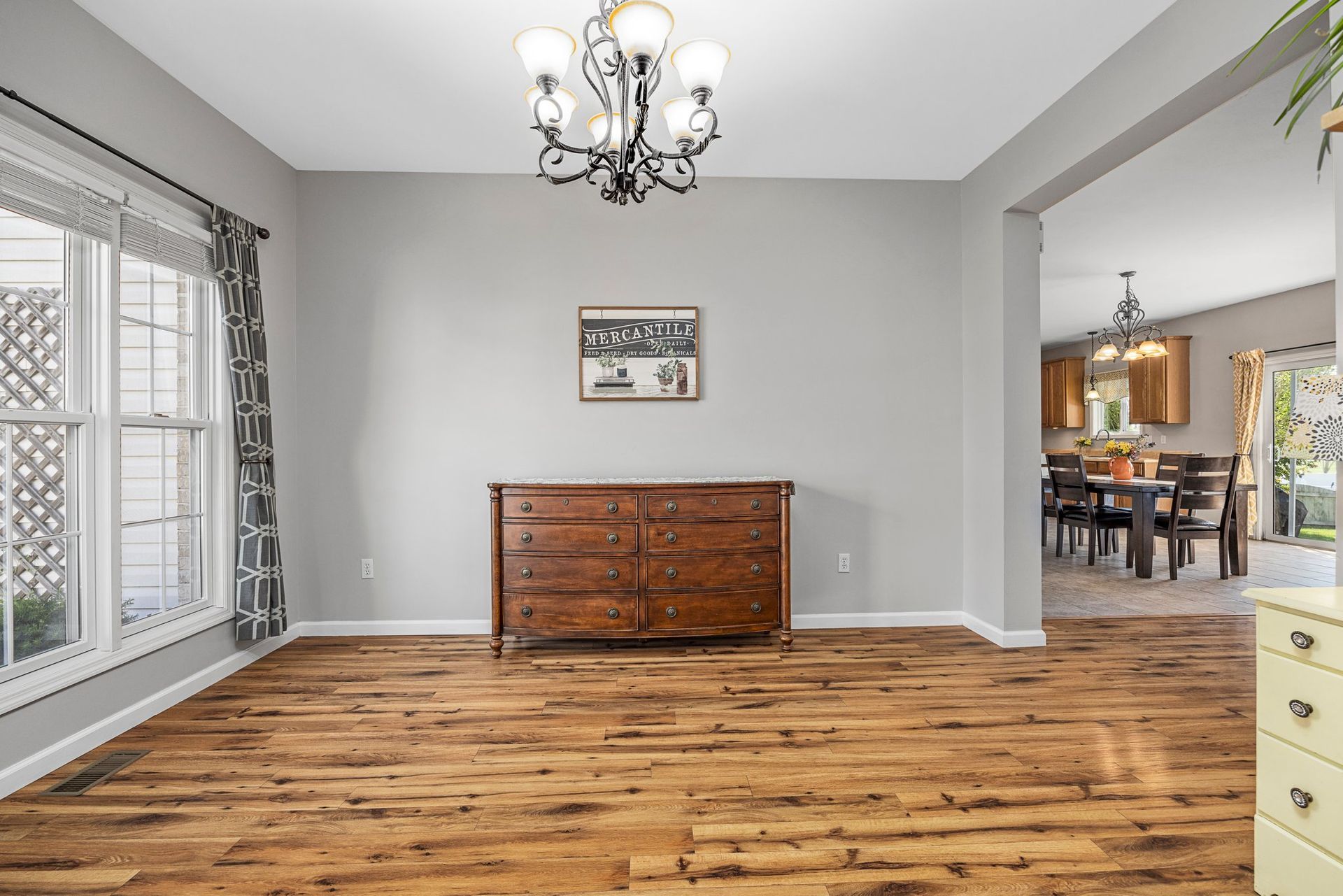 A dining room with hardwood floors , a dresser and a chandelier.