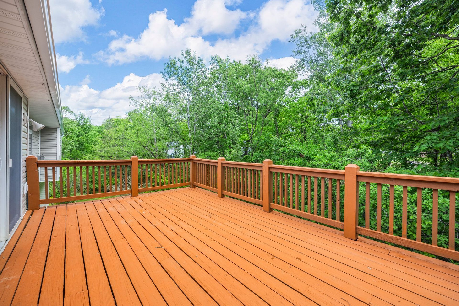 An empty wooden deck with a wooden railing and trees in the background.