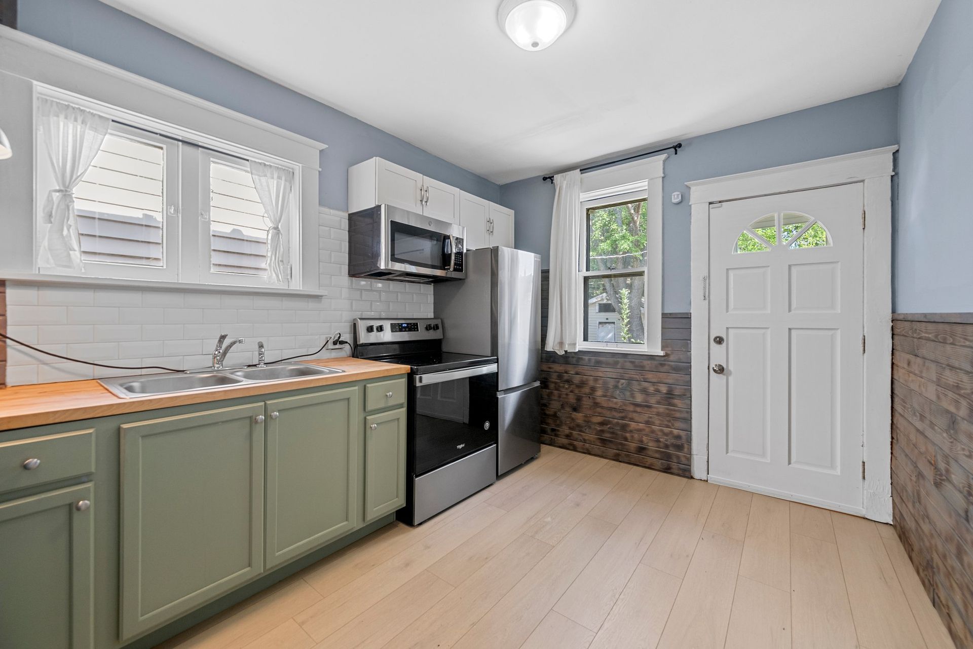 A kitchen with a stove , refrigerator , microwave and sink.