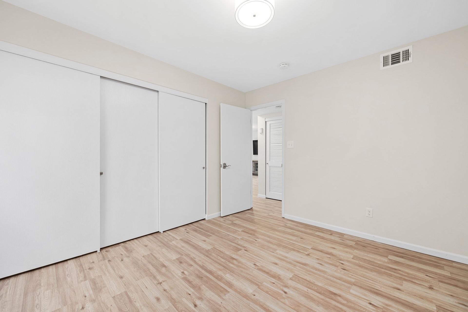 An empty bedroom with hardwood floors and white walls.