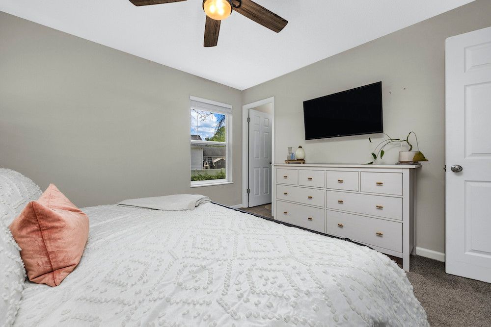 A bedroom with a bed , dresser , television and ceiling fan.