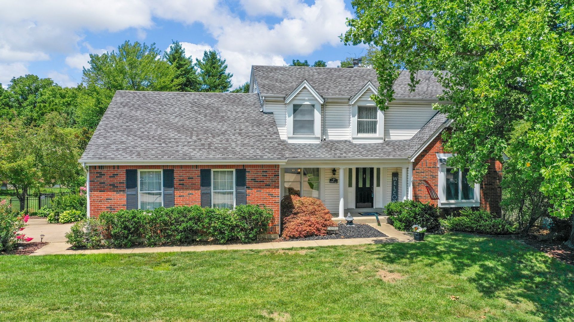 A large brick house with a gray roof and black shutters is for sale.