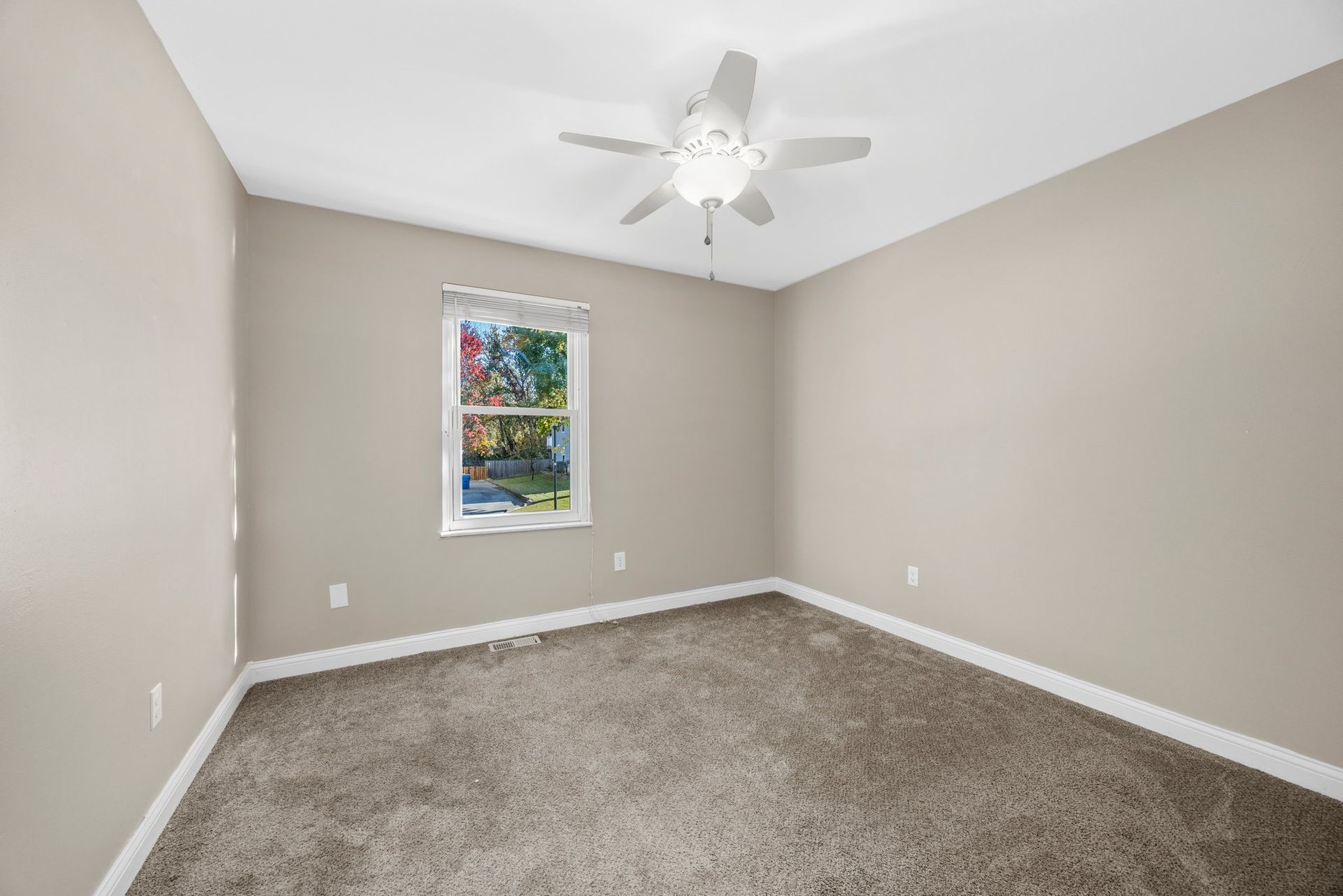 An empty bedroom with a ceiling fan and a window.
