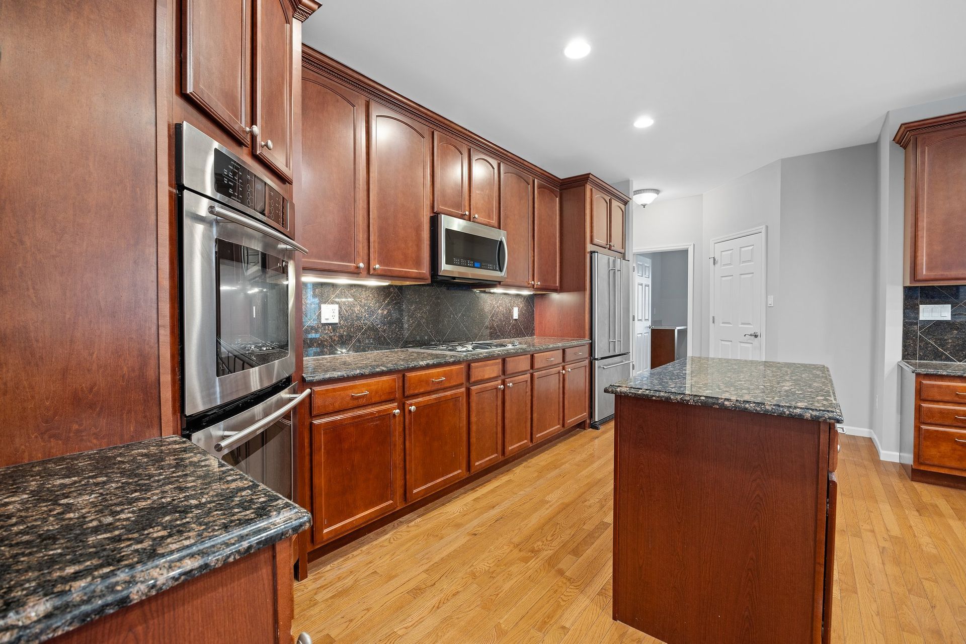 A kitchen with wooden cabinets , granite counter tops , stainless steel appliances and a large island.