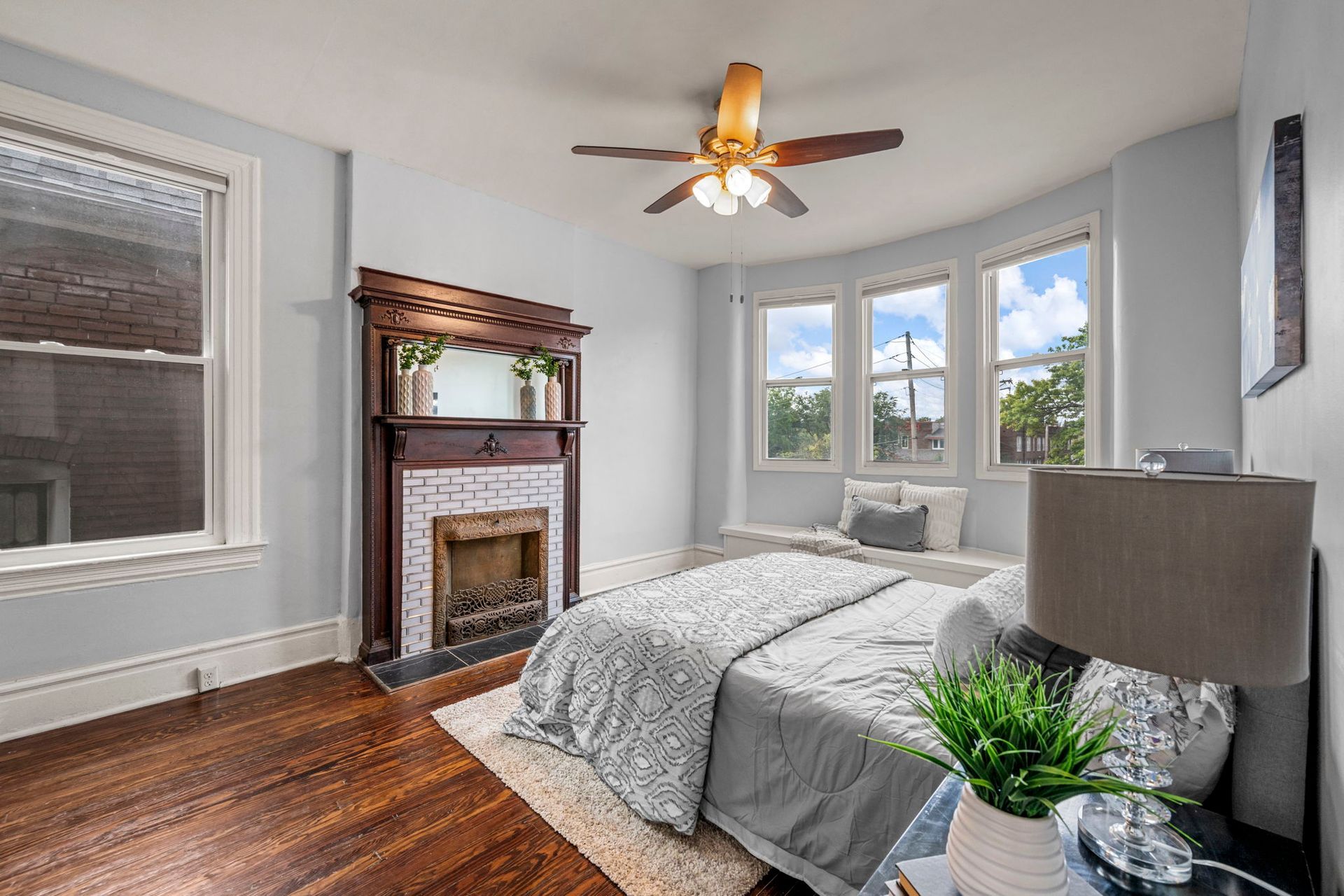 Bedroom with a bed, fireplace, and bay window with a built-in seat. Light blue walls and dark wood floors.
