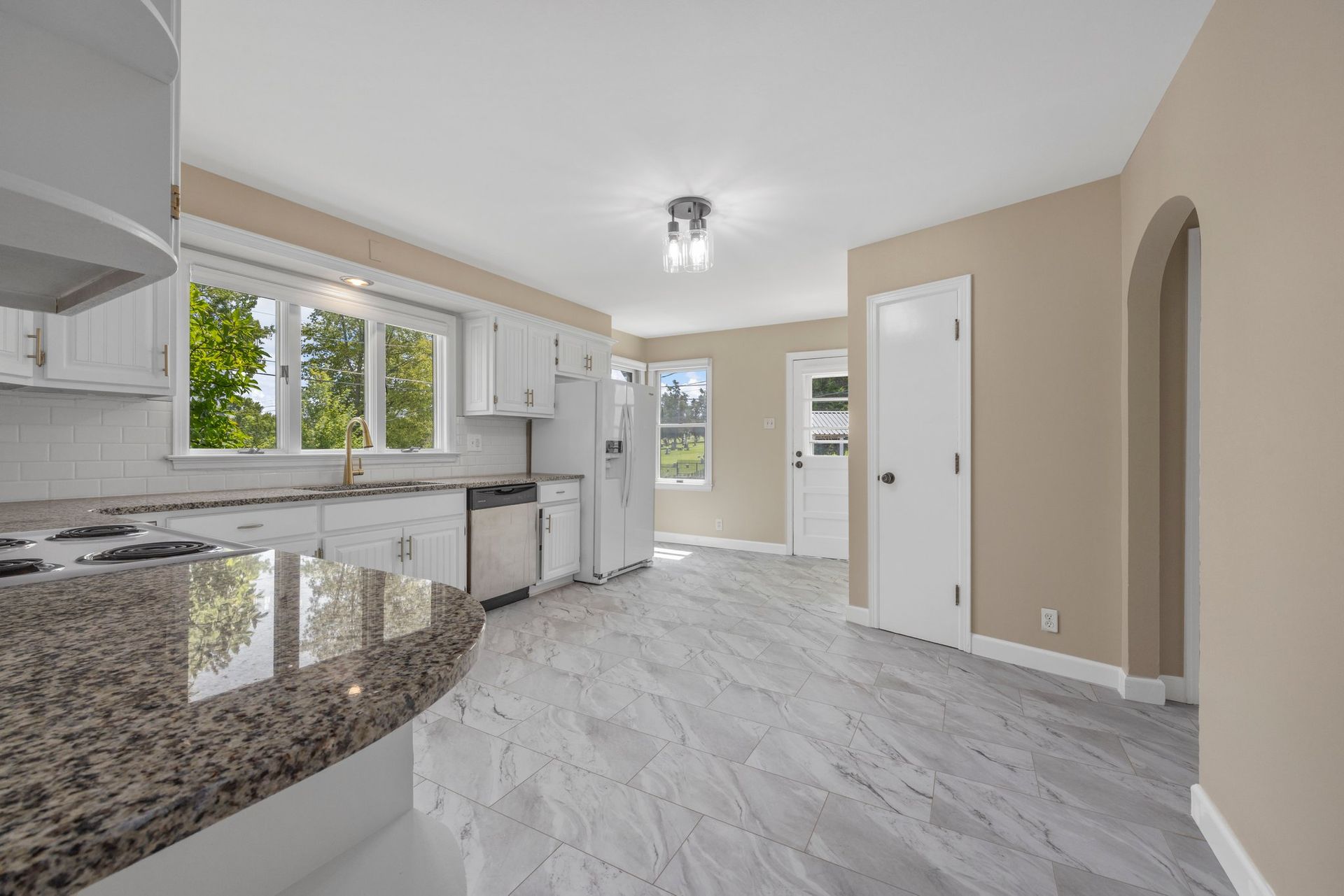 An empty kitchen with a granite counter top and white cabinets.
