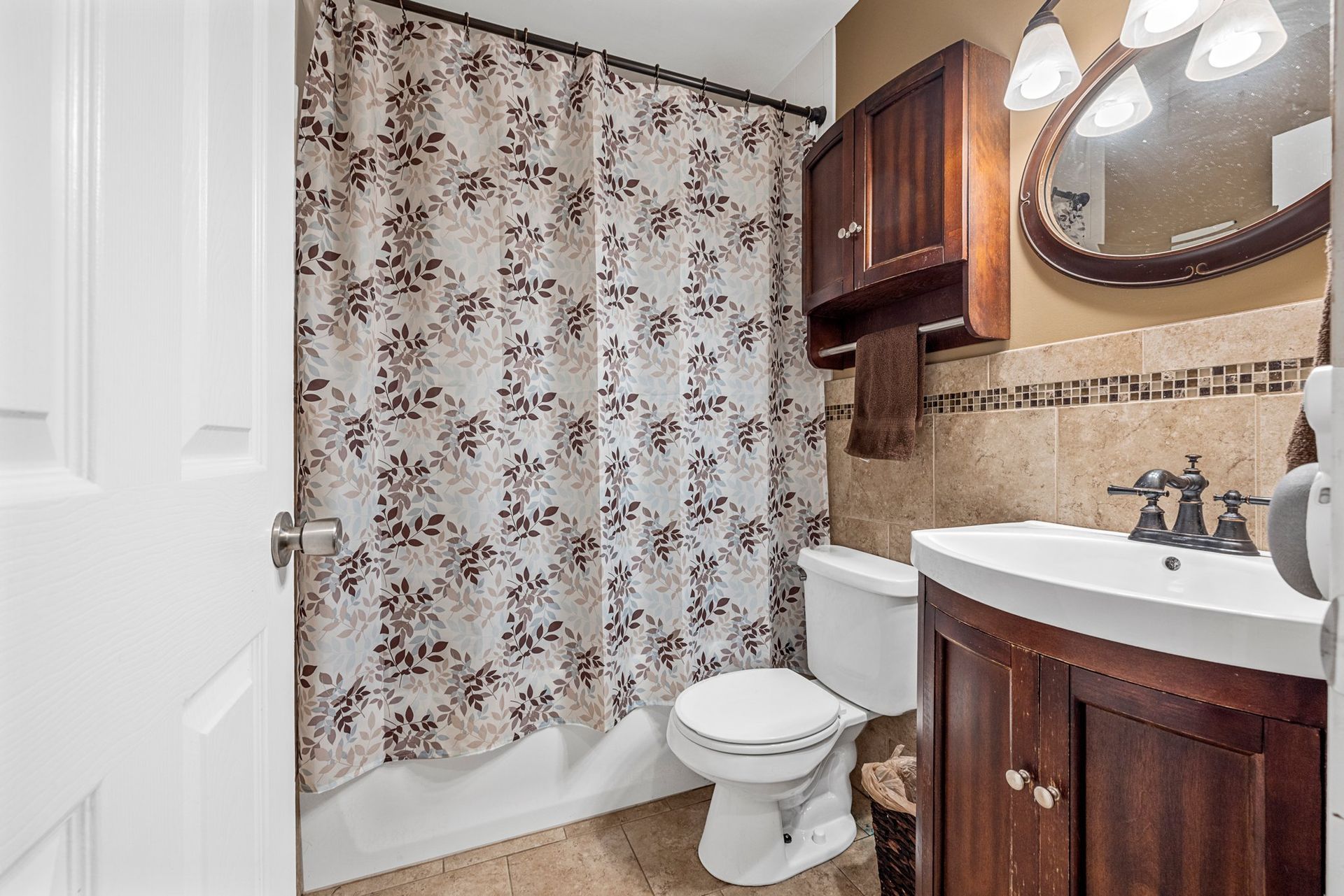 A bathroom with a toilet , sink , mirror and shower curtain.