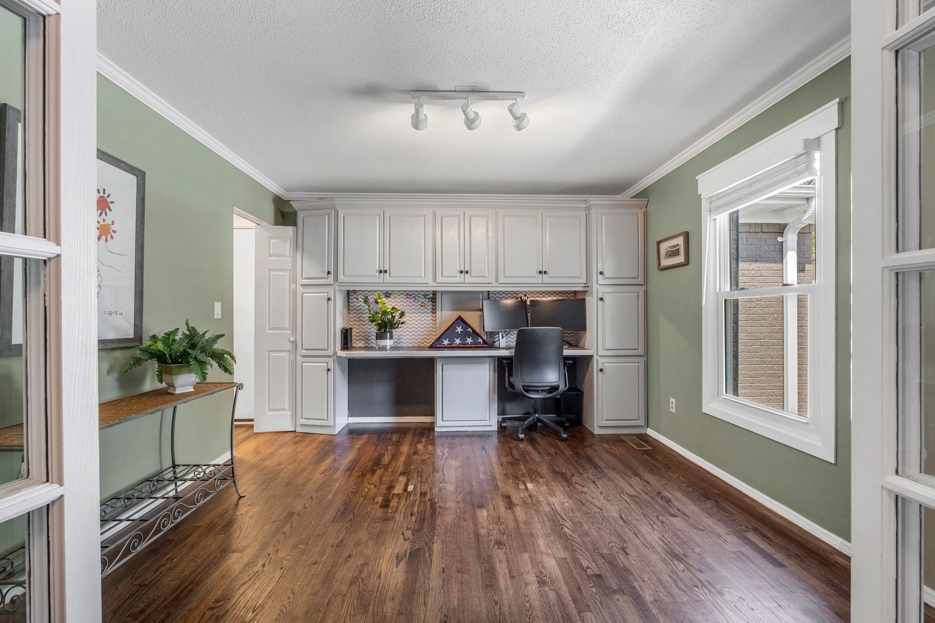 A living room with hardwood floors , white cabinets and a desk.