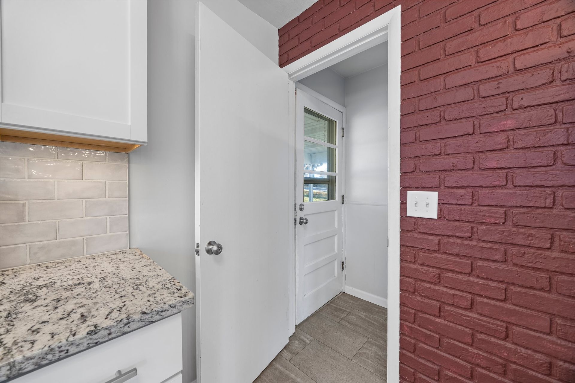 A kitchen with a red brick wall and a white door.