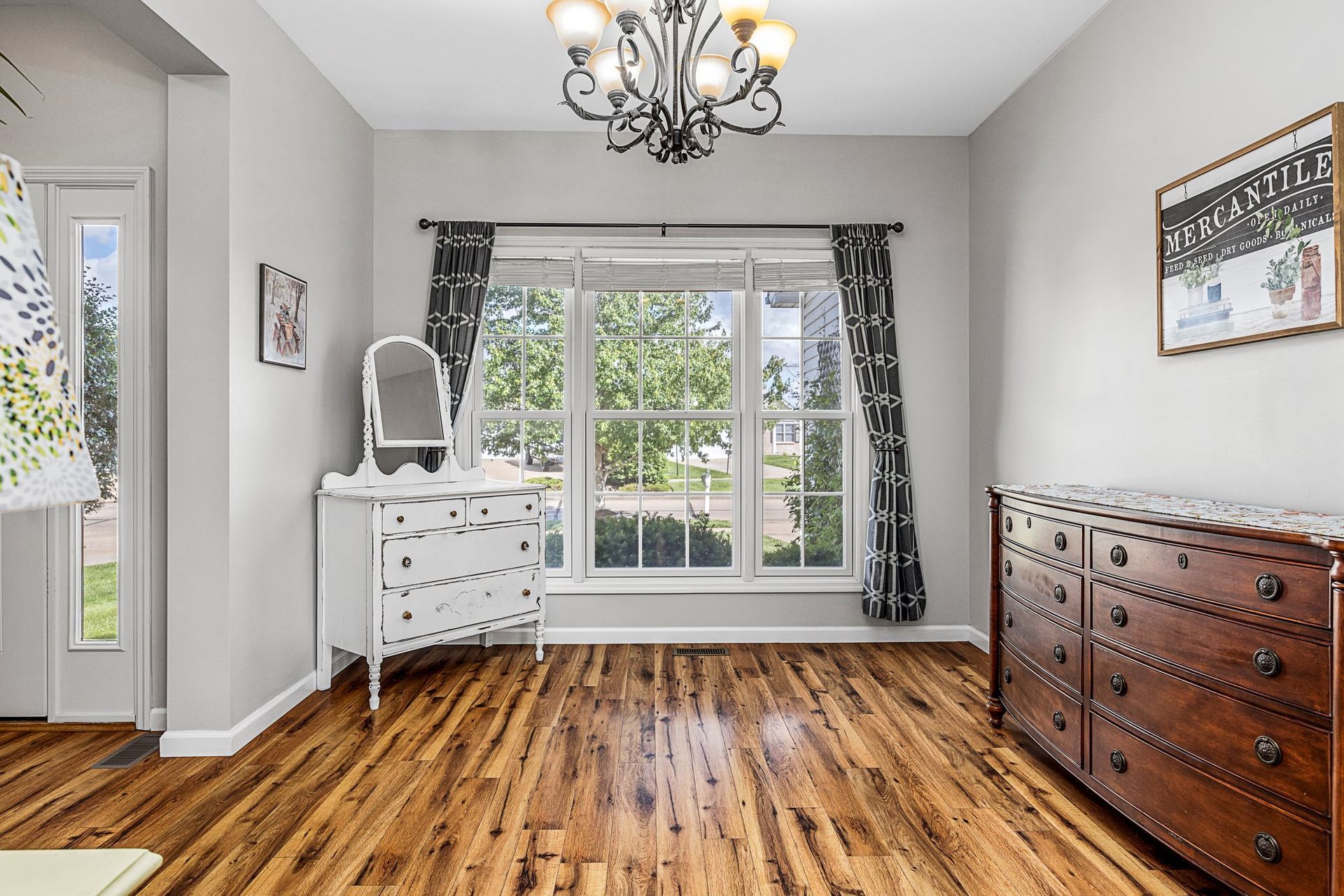 A bedroom with hardwood floors , a dresser , a mirror and a chandelier.