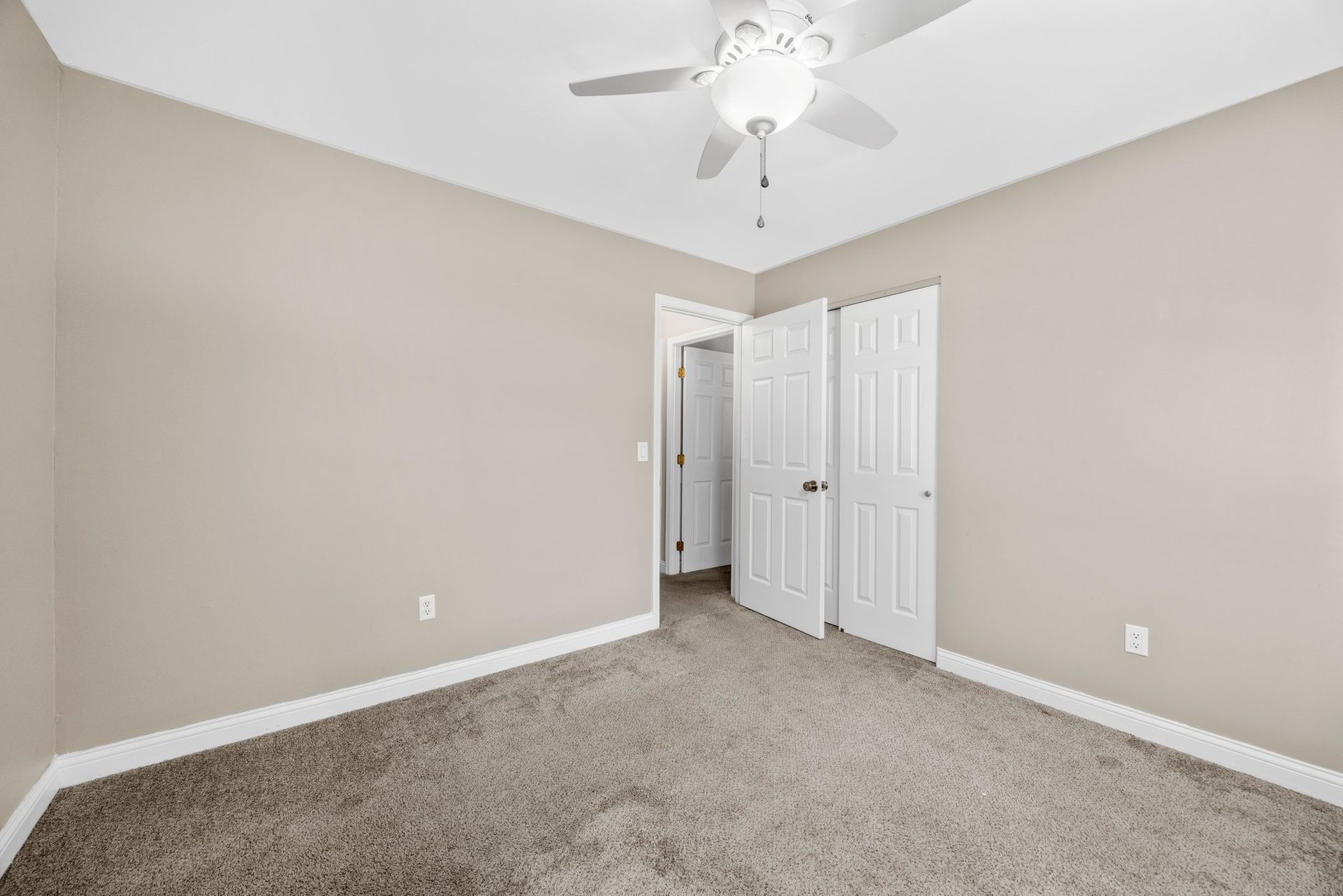 An empty bedroom with a ceiling fan and a carpeted floor.