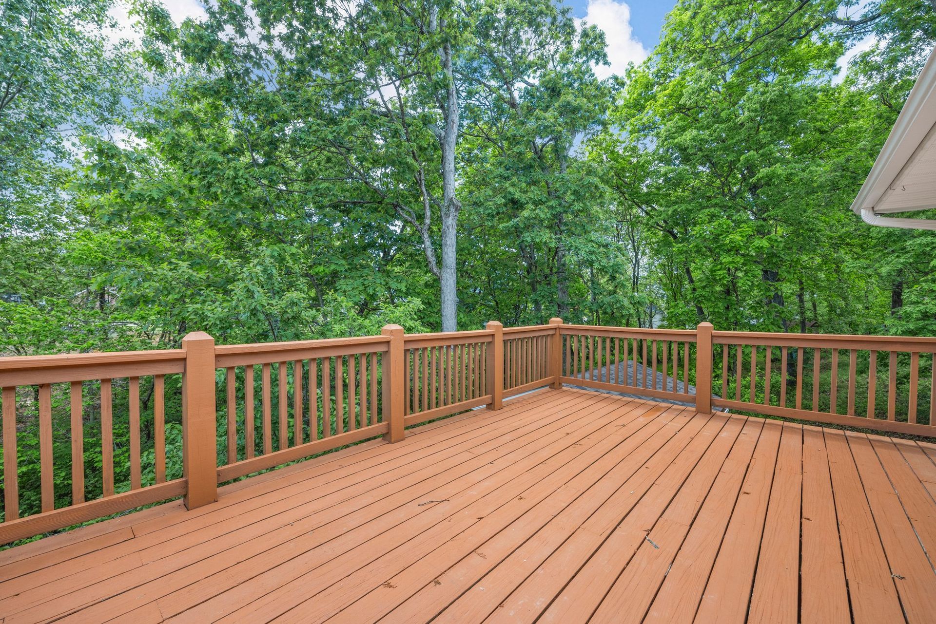 A large wooden deck with a railing and trees in the background.