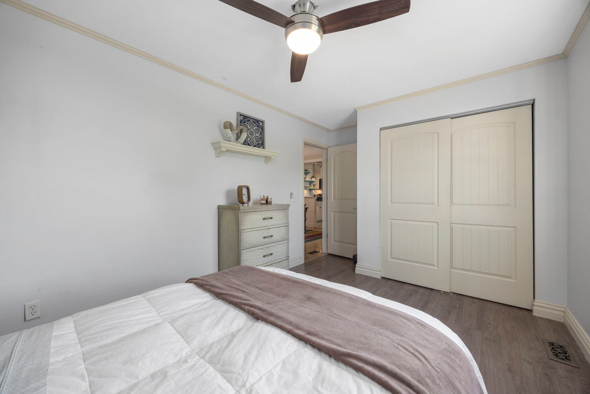 Bedroom with bed, dresser, closet, and open doorway to kitchen. Gray walls, wood floor.