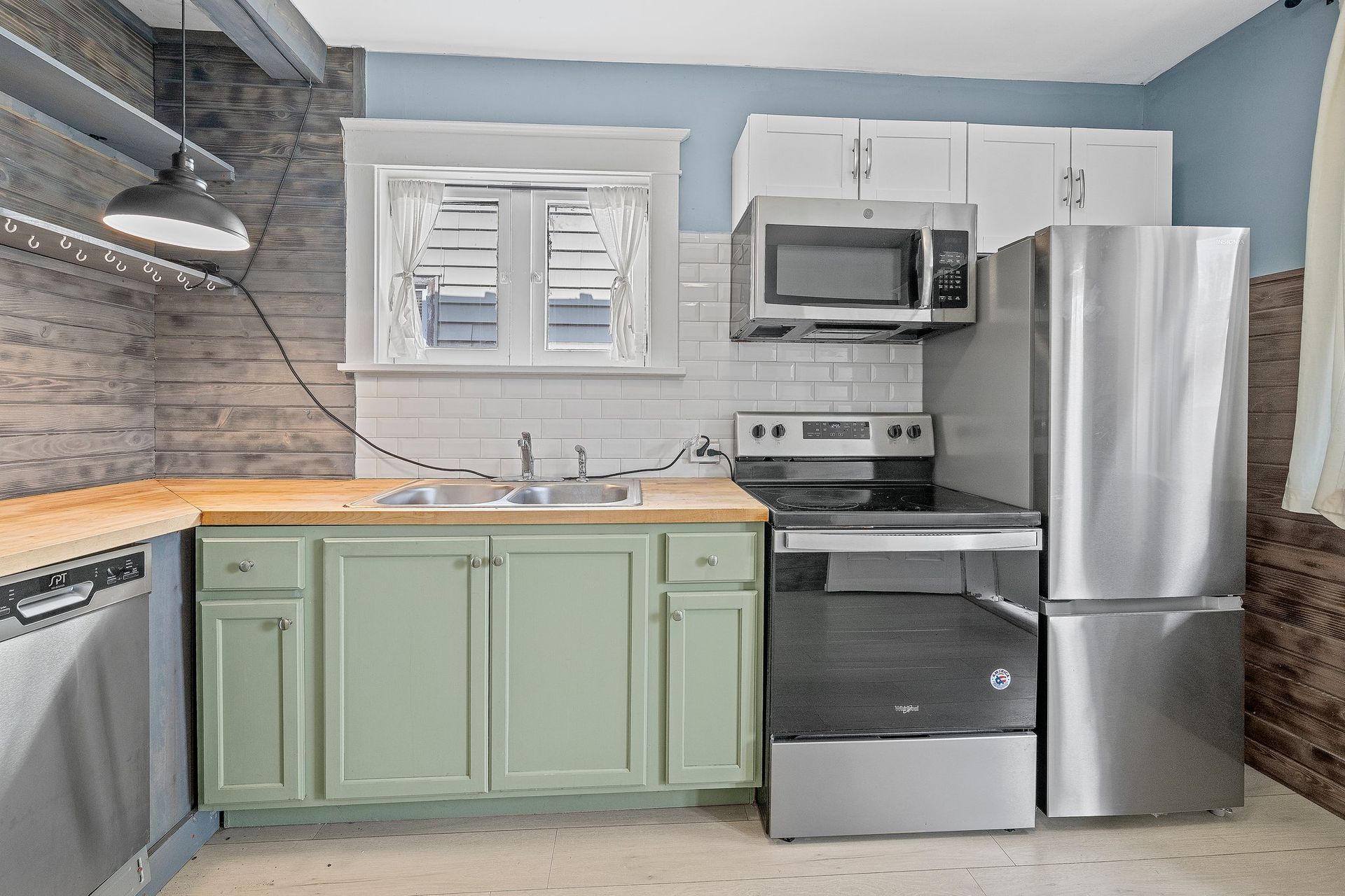 A kitchen with stainless steel appliances and green cabinets.