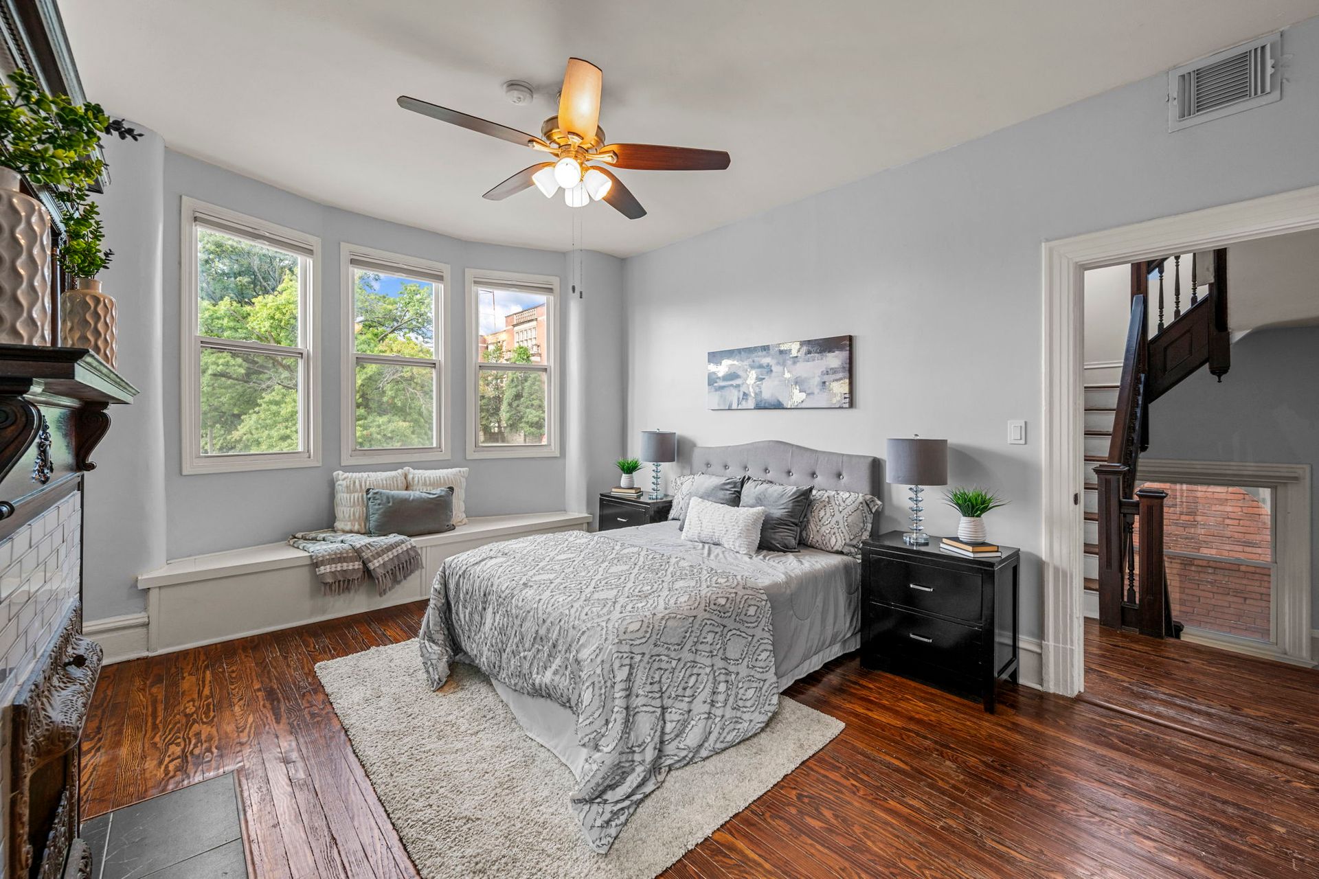 Bedroom with gray walls, bed, and window seat; dark wood floors. Doorway to stairs.