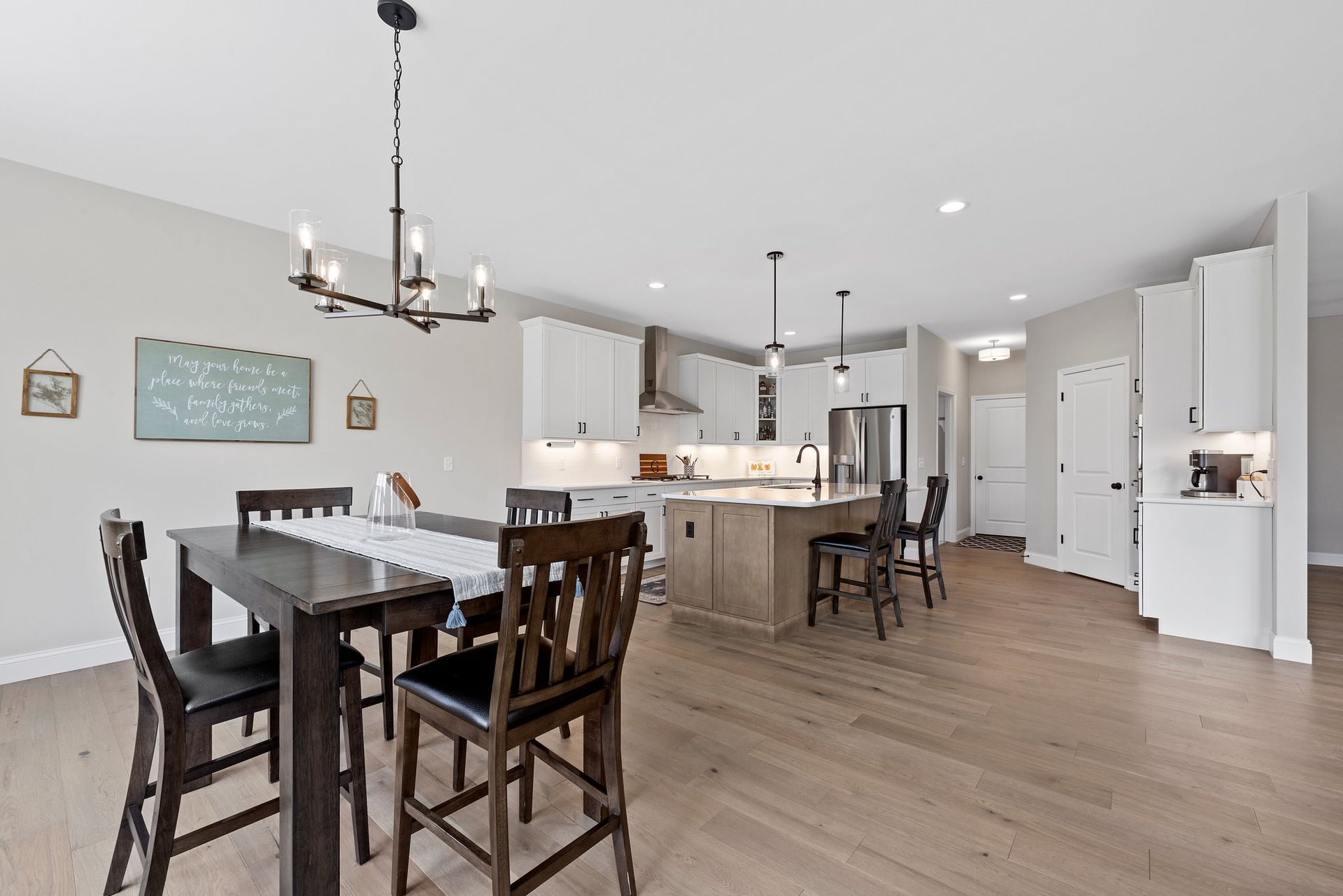 A dining room with a table and chairs and a kitchen in the background.