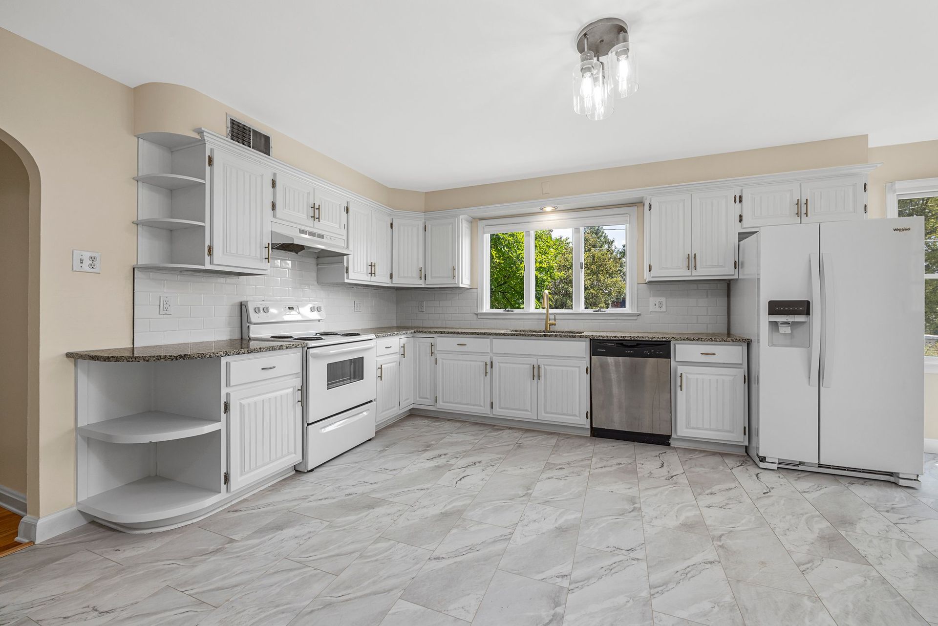 An empty kitchen with white cabinets , stainless steel appliances , a refrigerator and a dishwasher.
