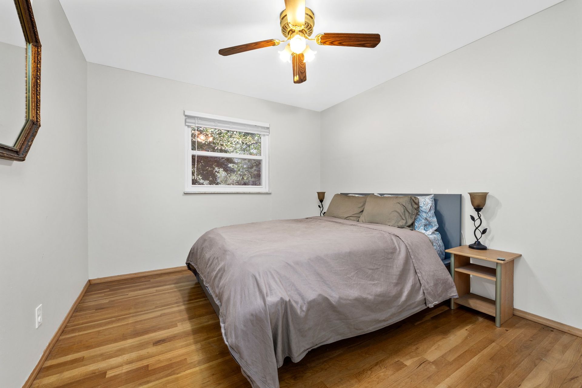A bedroom with a bed , nightstand , mirror and ceiling fan.