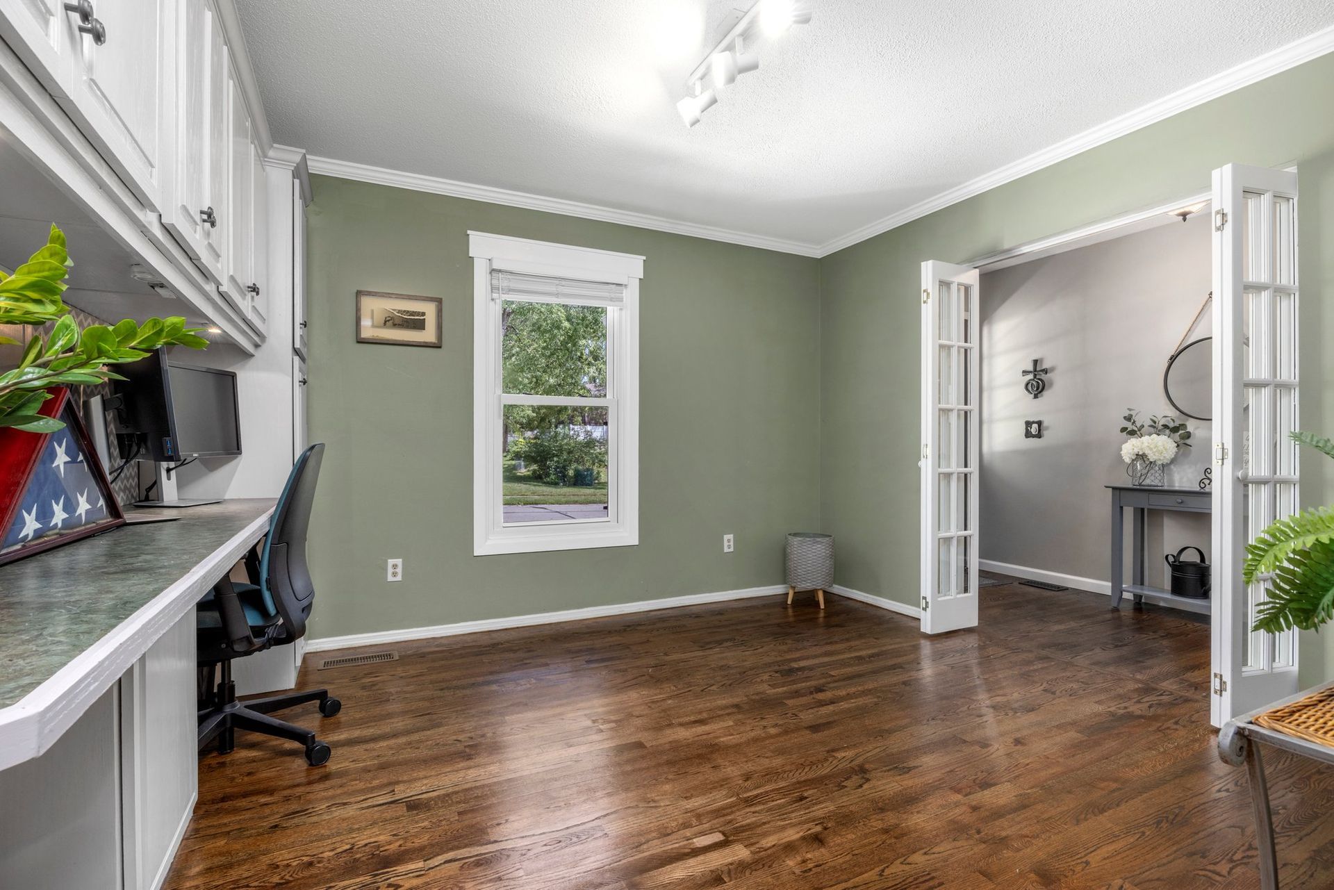 A living room with hardwood floors , green walls , a desk and a chair.