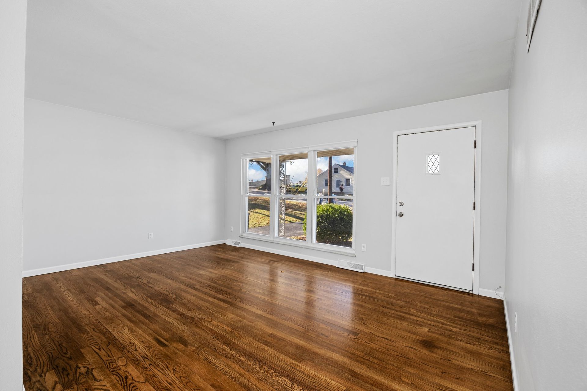 An empty living room with hardwood floors and white walls.