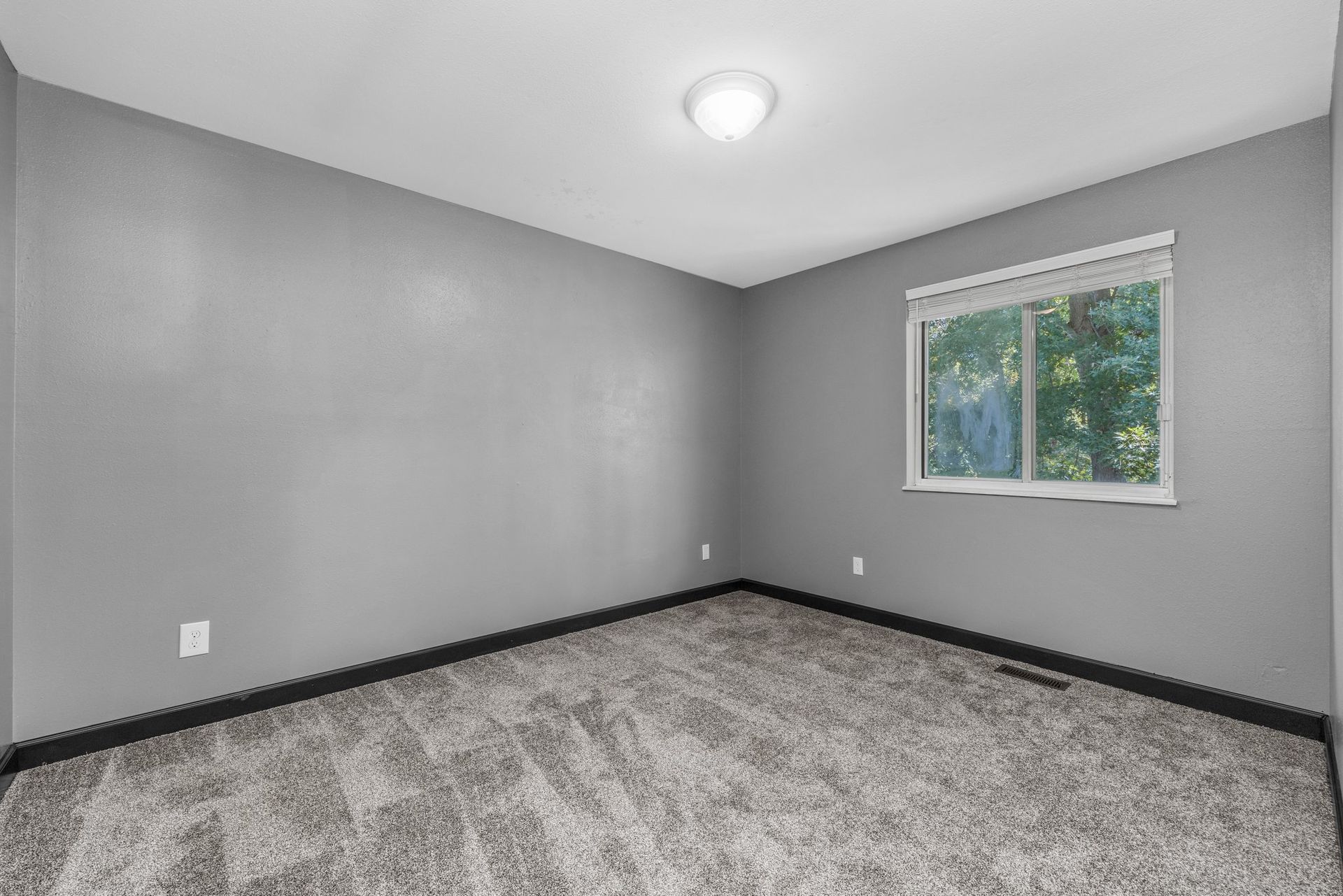 An empty bedroom with a gray carpet and a window.