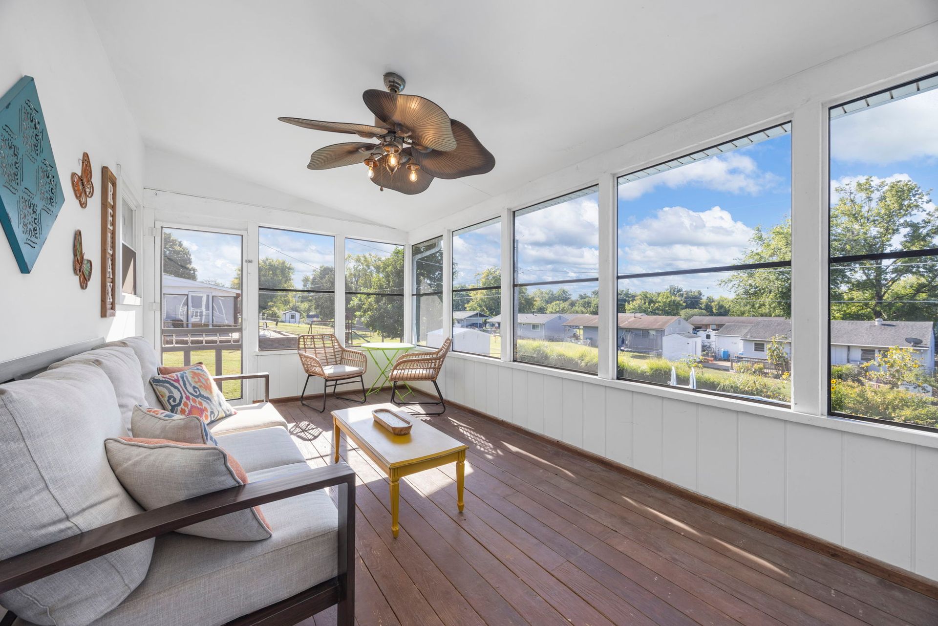Sunroom with brown wood floor, white walls, and large windows overlooking a sunny neighborhood.