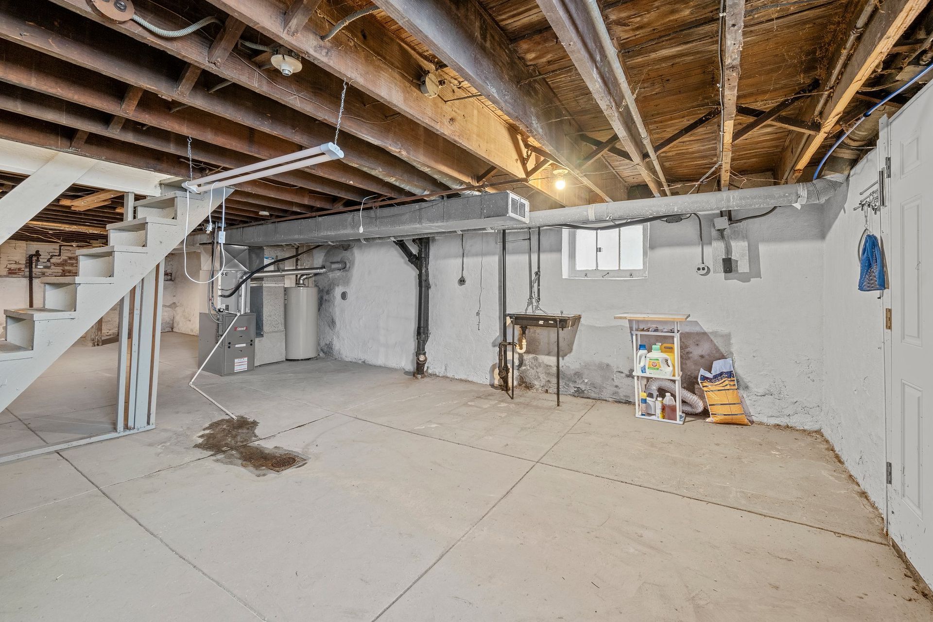 A basement with a staircase and a sink in it.