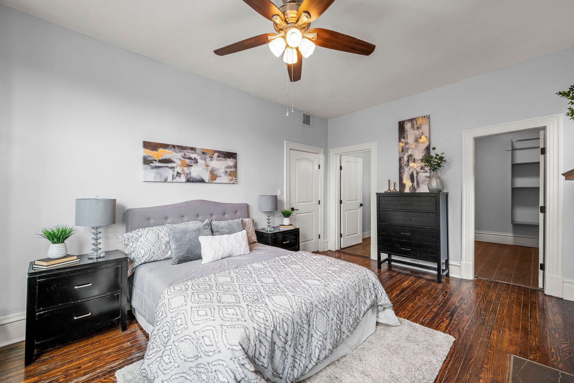 Bedroom with bed, dark furniture, two doors, artwork, wood floor, and ceiling fan.
