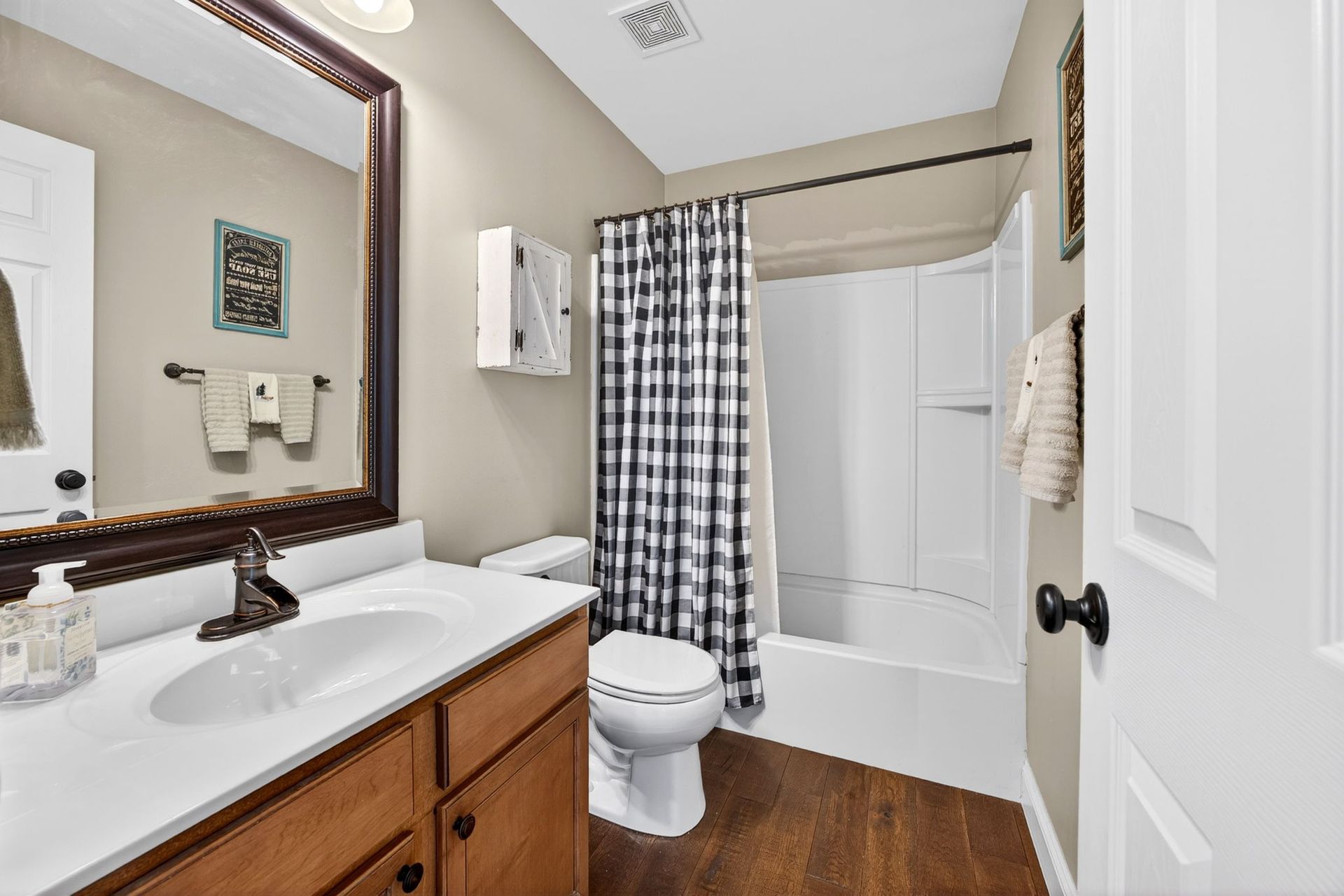 A bathroom featuring a wooden vanity with a white countertop, a toilet, and a bathtub with a black-and-white curtain.