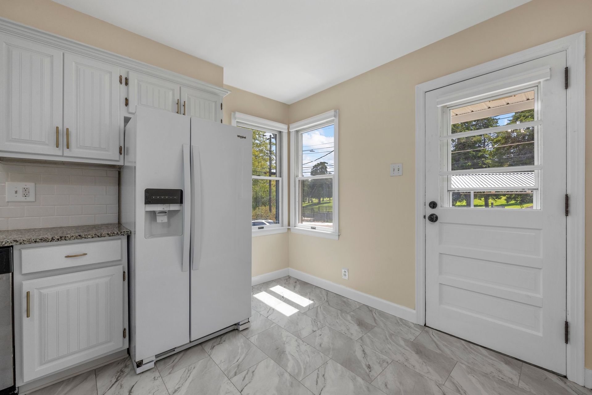 A kitchen with white cabinets , a refrigerator and a window.