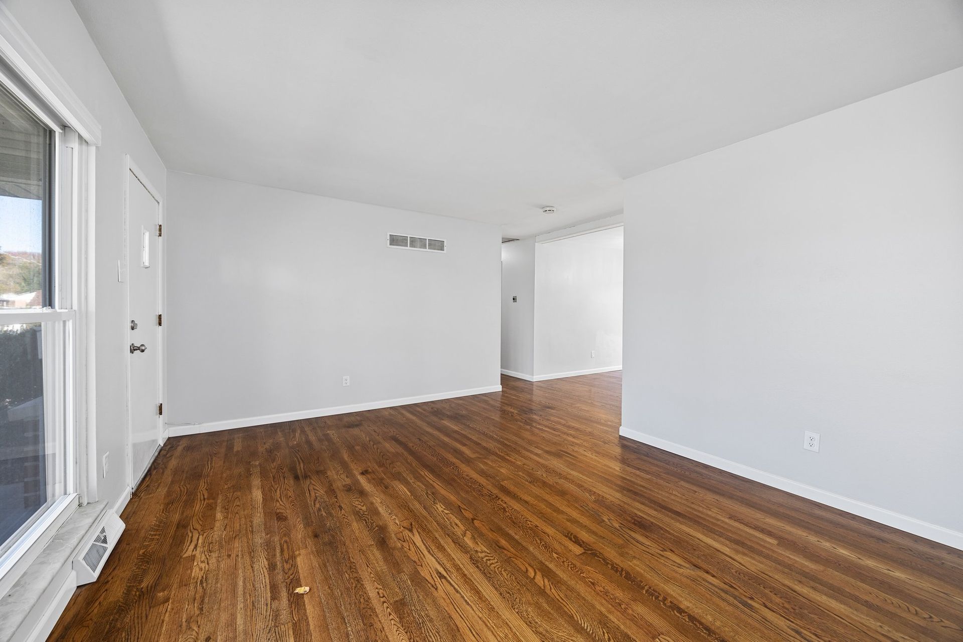 An empty living room with hardwood floors and white walls.
