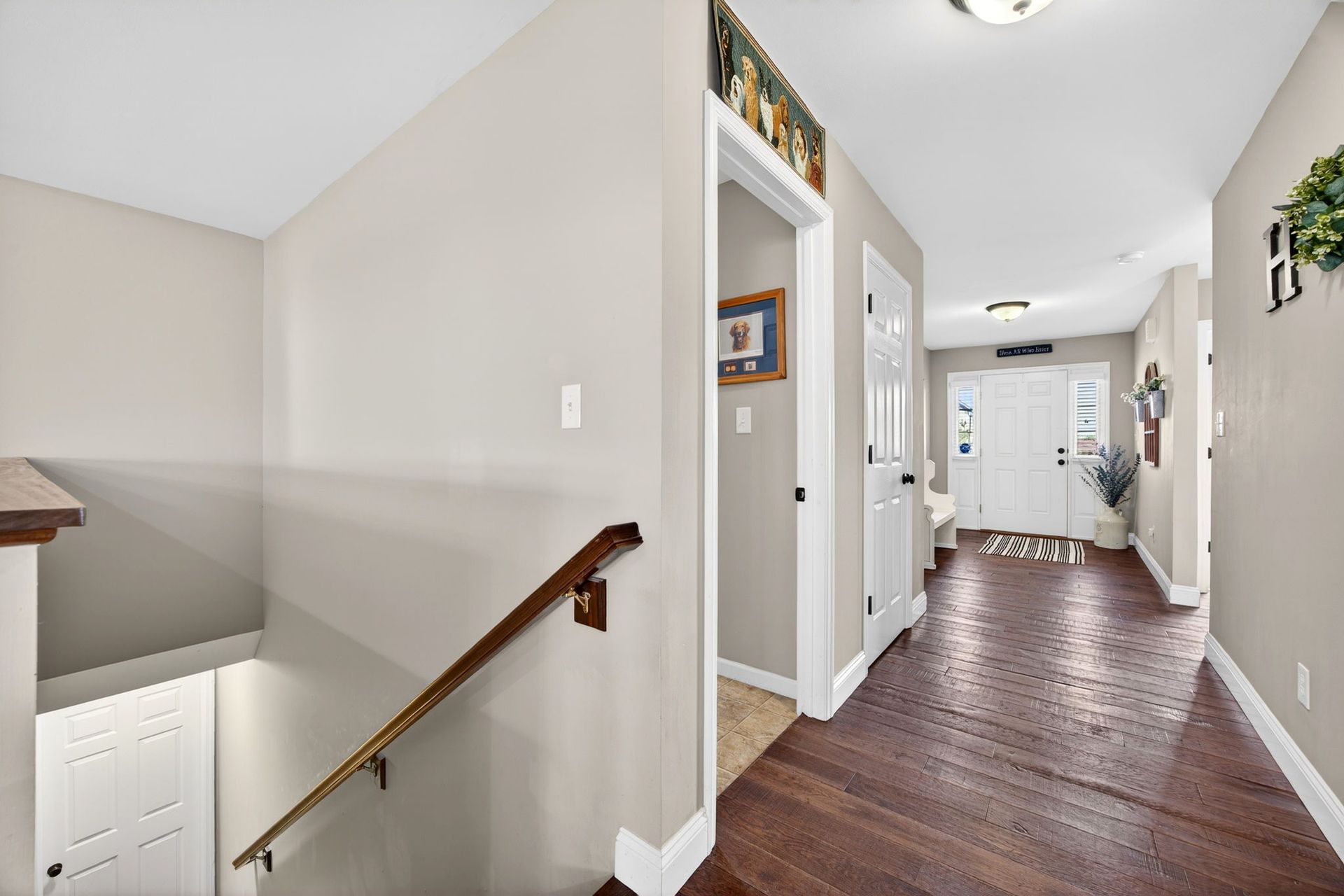 An interior hallway with light gray walls, dark wood flooring, and a staircase leading down to a white door.