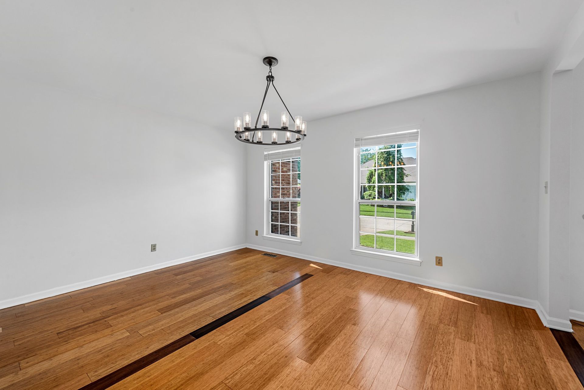 An empty living room with hardwood floors and a chandelier hanging from the ceiling.