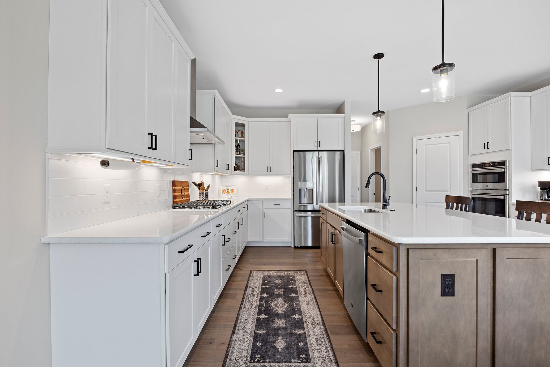 A kitchen with white cabinets , stainless steel appliances , a large island and a rug.