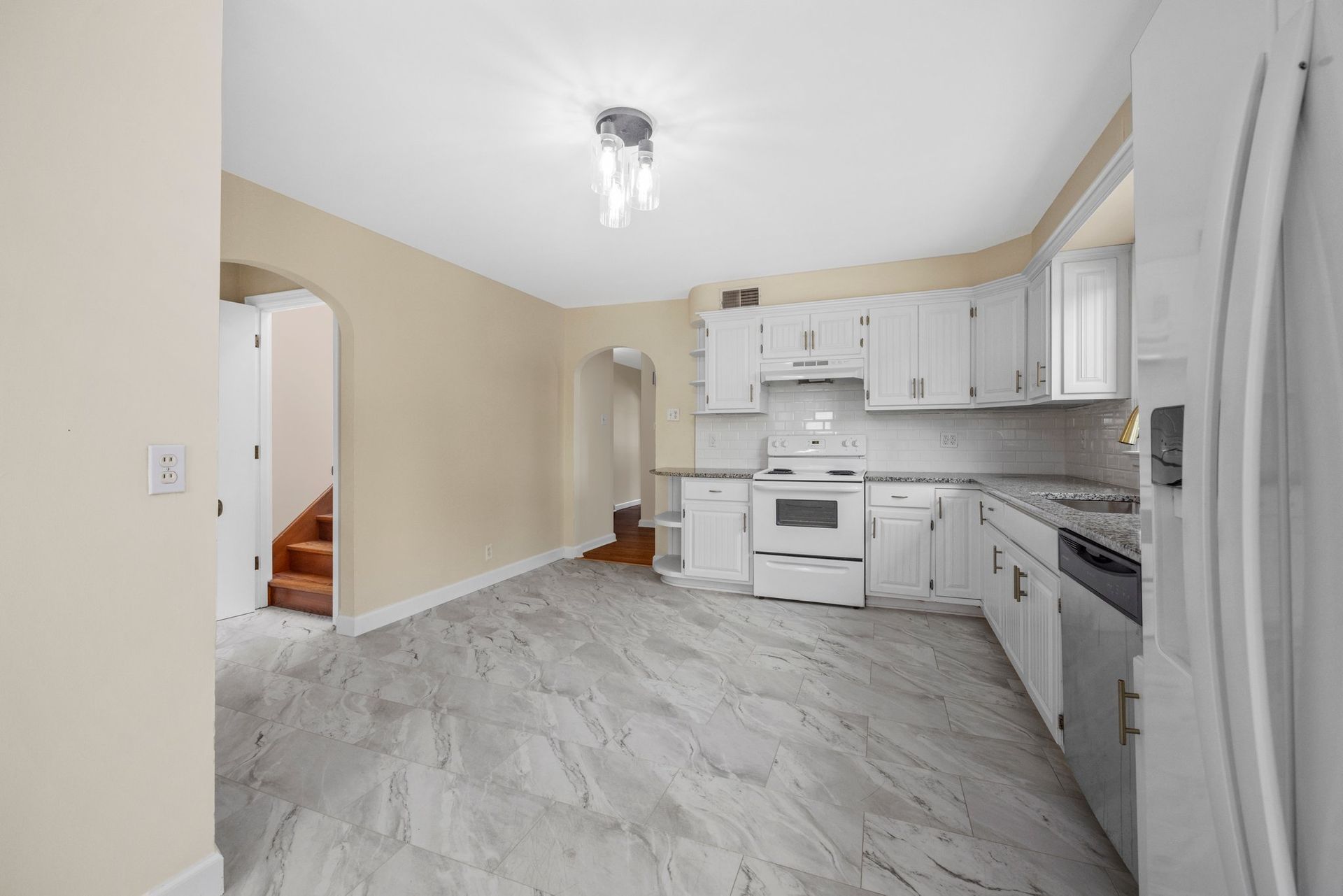 An empty kitchen with white cabinets and a refrigerator.
